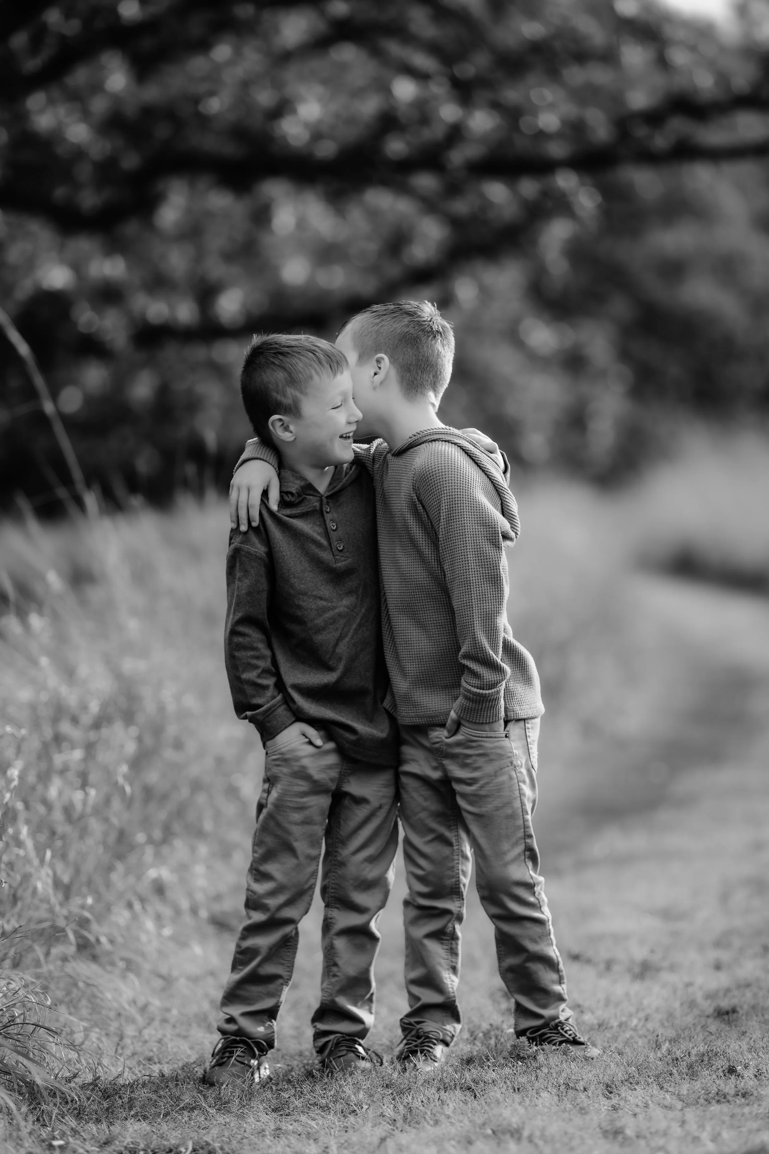 Two boys sharing a hug and whispering to each other outdoors in Sioux Falls, South Dakota at Good Earth State Park.