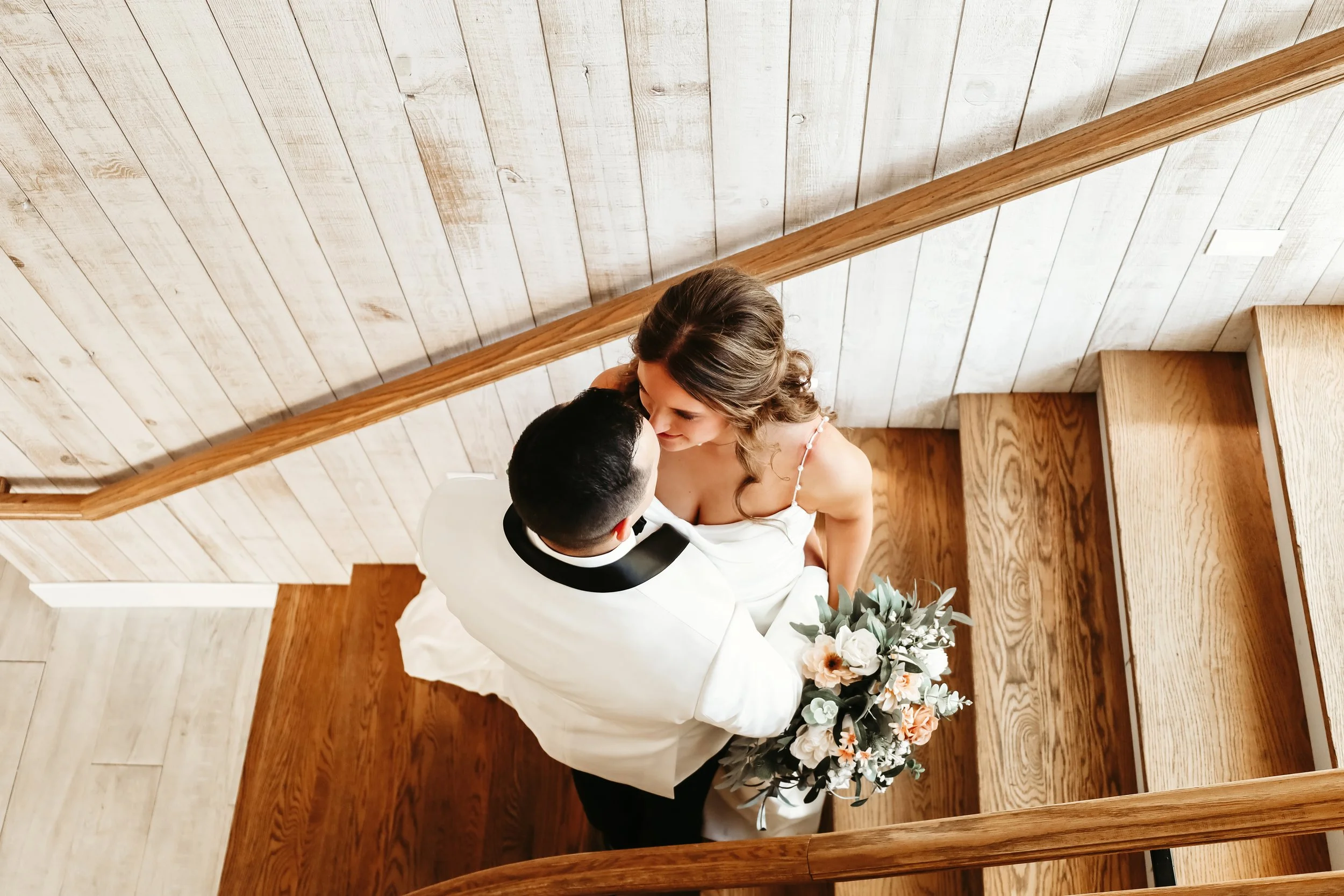 A bride and groom sharing a kiss on a staircase at their wedding, with the bride holding a bouquet of flowers at Laurel Ridge in Sioux Falls SD.