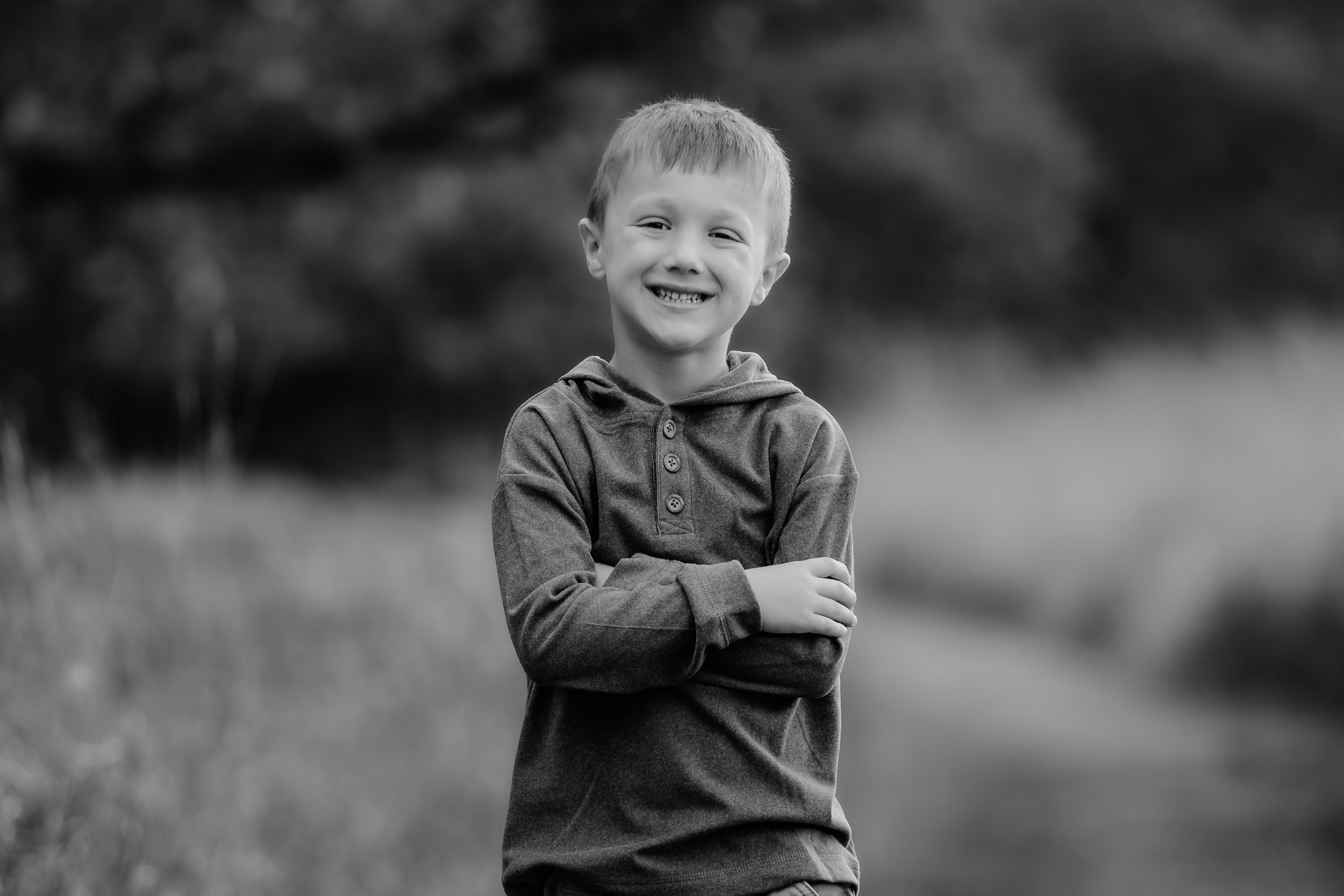 Black and white photo of smiling young boy with crossed arms outdoors in Sioux Falls, South Dakota at Good Earth State Park.