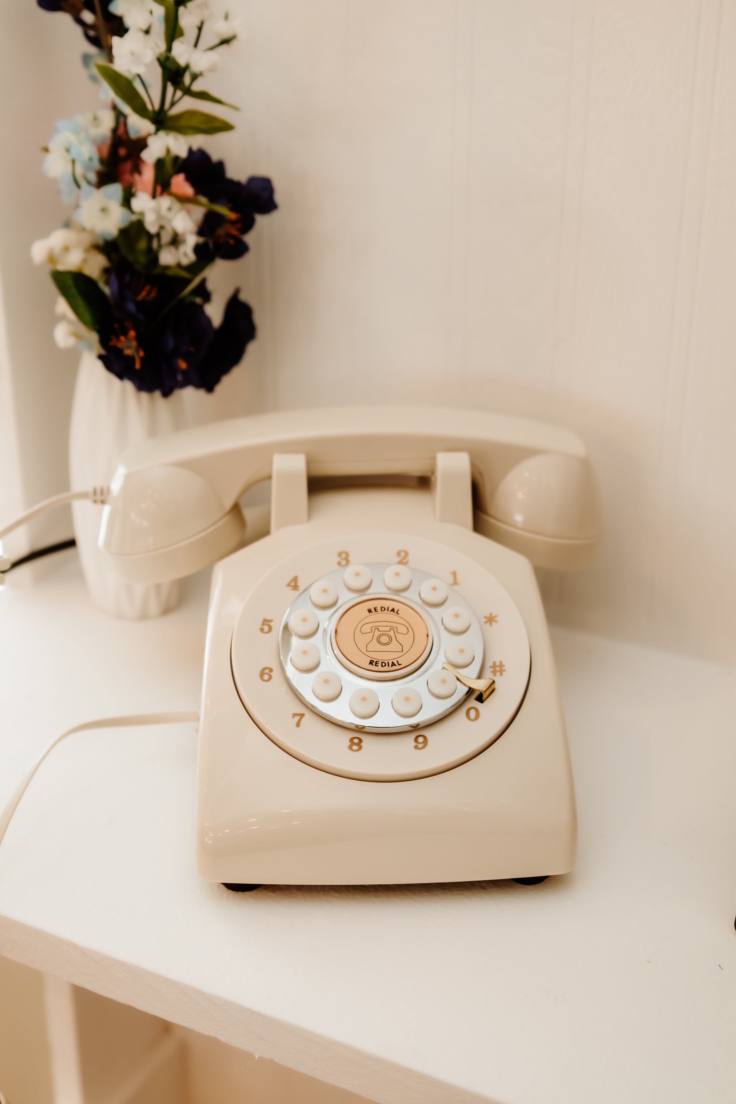 Vintage rotary dial telephone in cream color with a flower arrangement in a white vase in the background min Luverne, MN.
