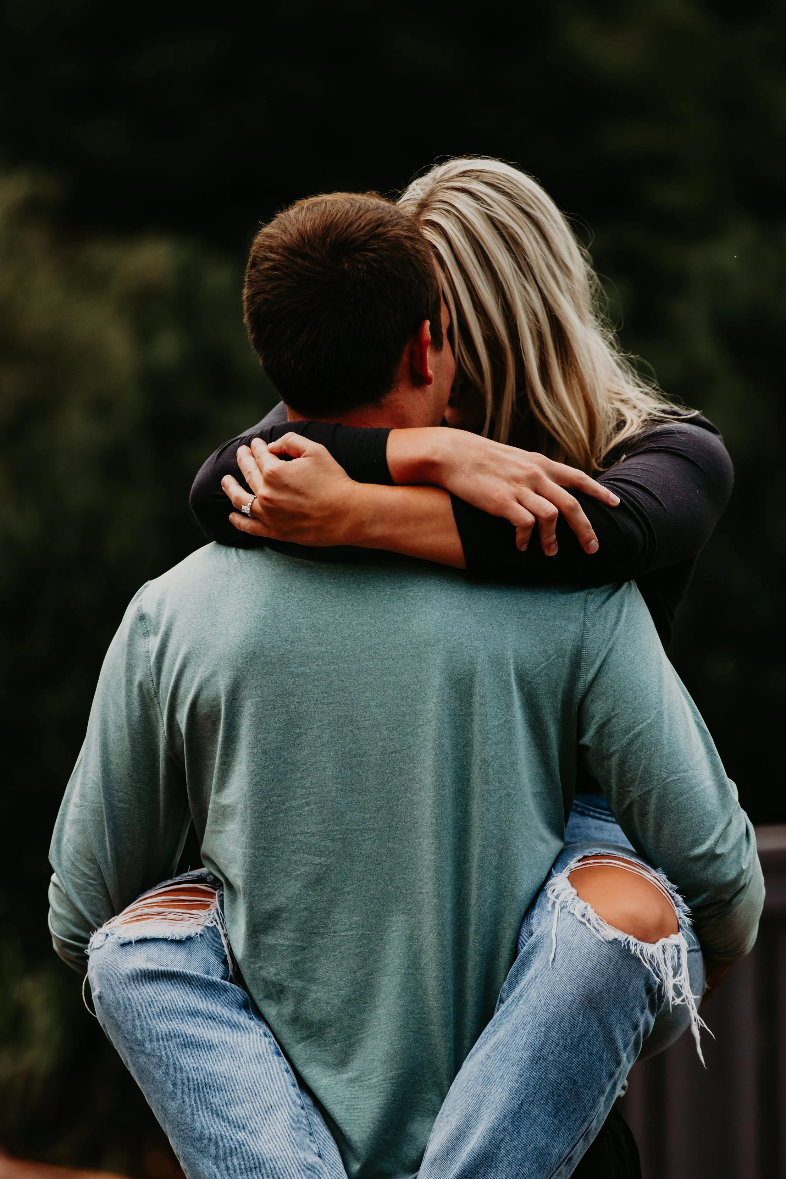 A couple sharing a kiss, with the woman sitting on the man's shoulders outdoors at sunset or dusk at Good Earth State Park in Sioux Falls, South Dakota.