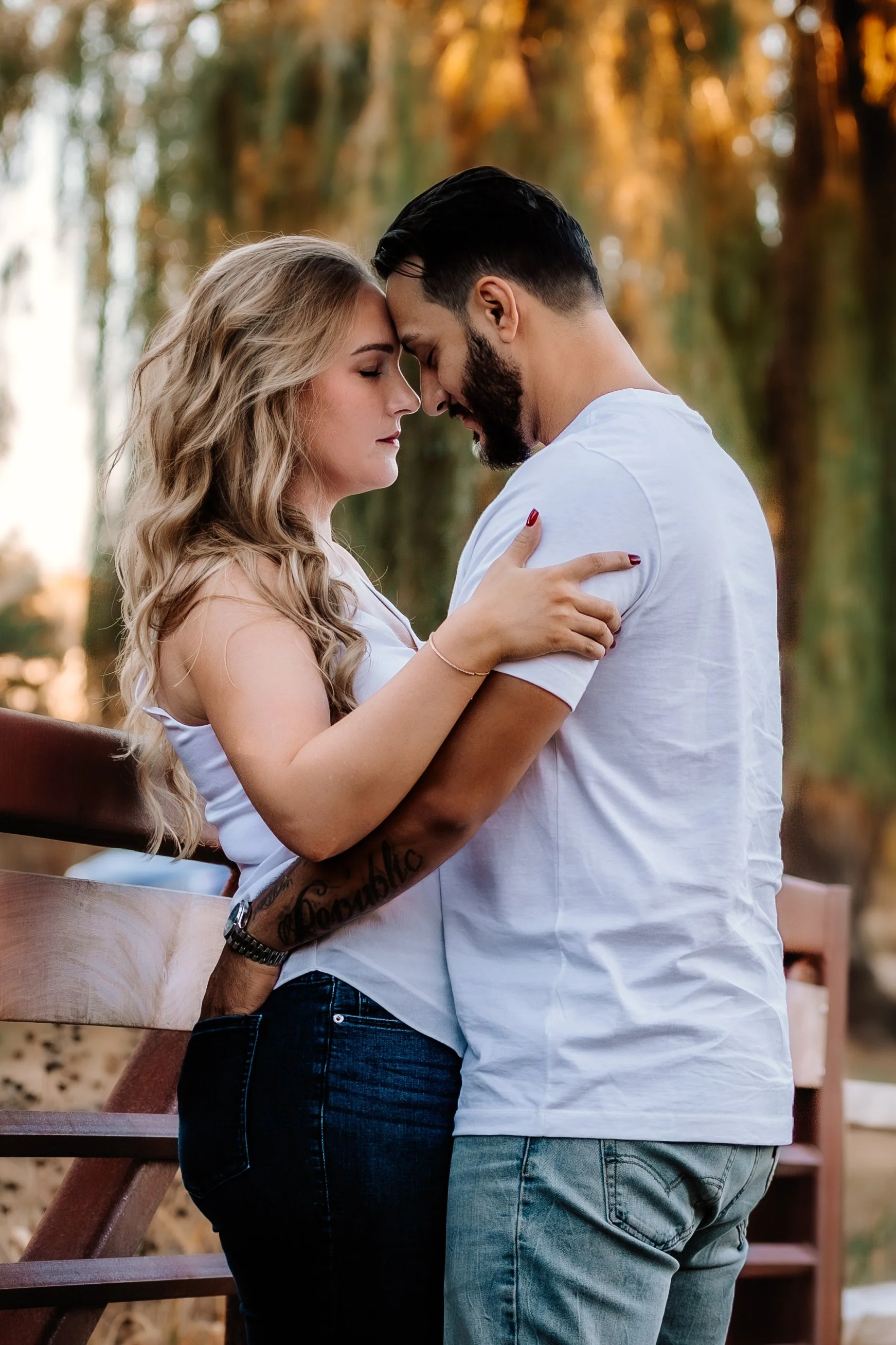 A couple stands close together with foreheads touching outdoors during sunset, embracing each other at Mary Jo Wegner Arboretum in Sioux Falls, South Dakota.