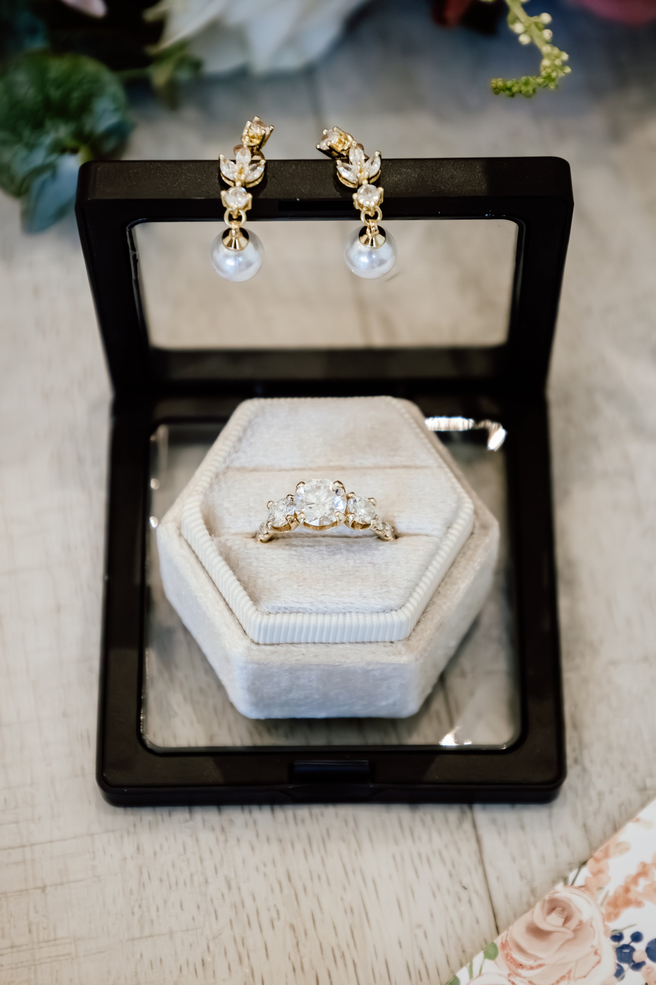 A jewelry box with a ring on a velvet cushion inside and a pair of pearl earrings hanging on top, on a light-colored wooden surface at Laurel Ridge in Sioux Falls SD.