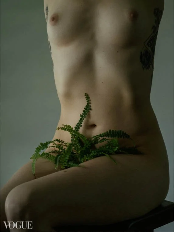 Photographie en plan serré sur le corps d'une femme blanche mince assise. Elle est étirée et son visage n'est pas visible, une fougère semble sortir d'entre ses jambes à la place des poils pubiens.