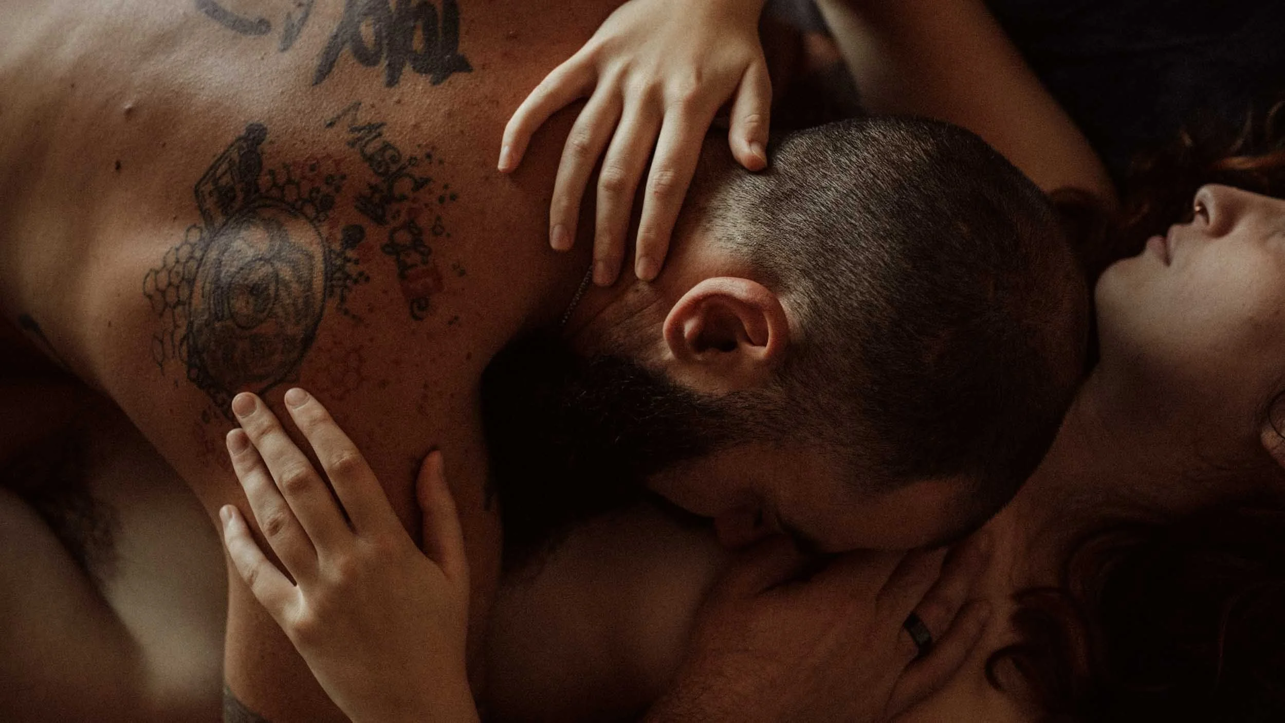Un homme et une femme allongés l'un sur l'autre, la femme enlace l'homme. Ses mains sont posés sur sa nuque et ses épaules.