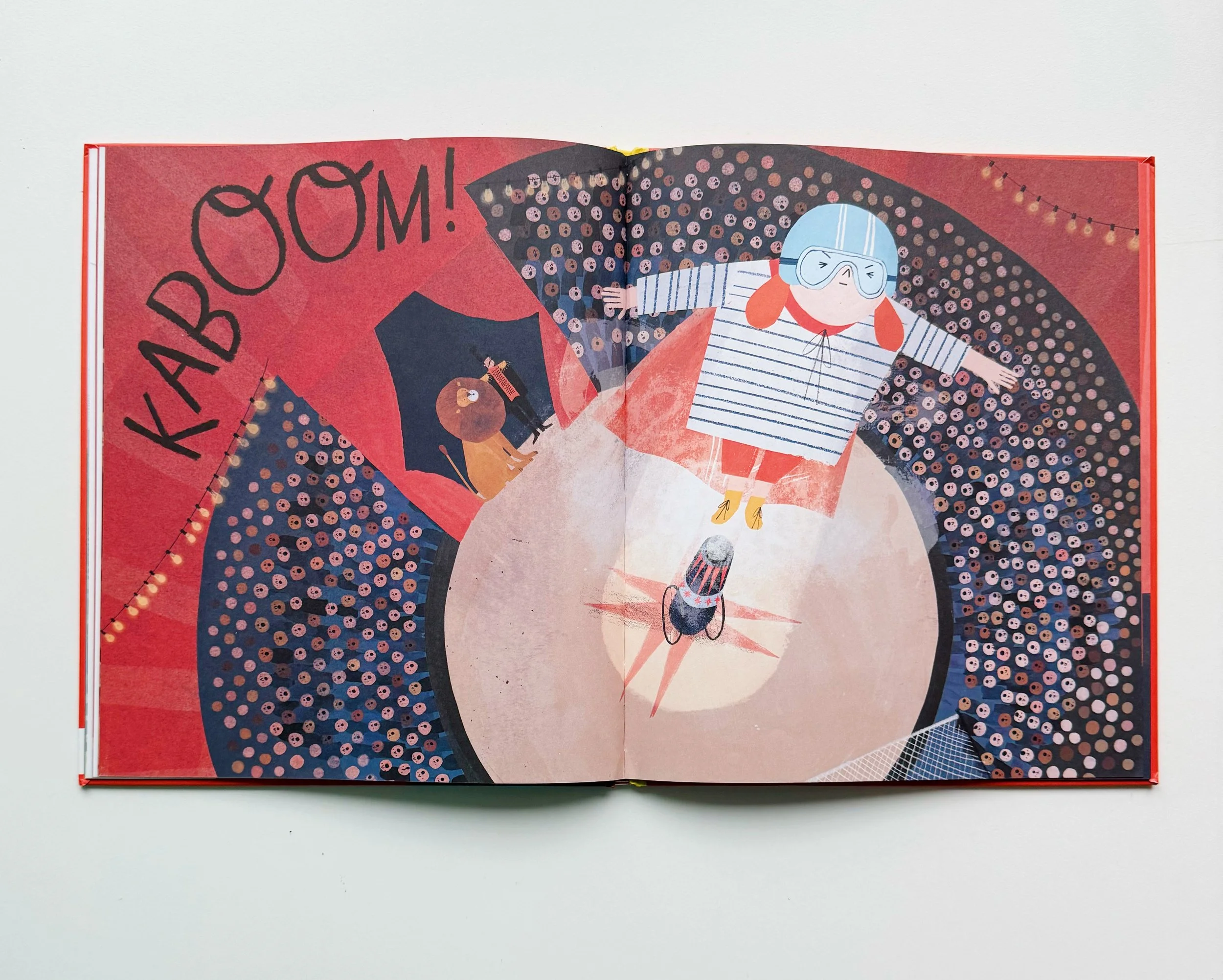 Open children's book illustration with a girl wearing goggles, striped shirt, and yellow boots, standing on a large letter 'O' with the word 'KABOOM!' written in large uppercase letters on the left side.