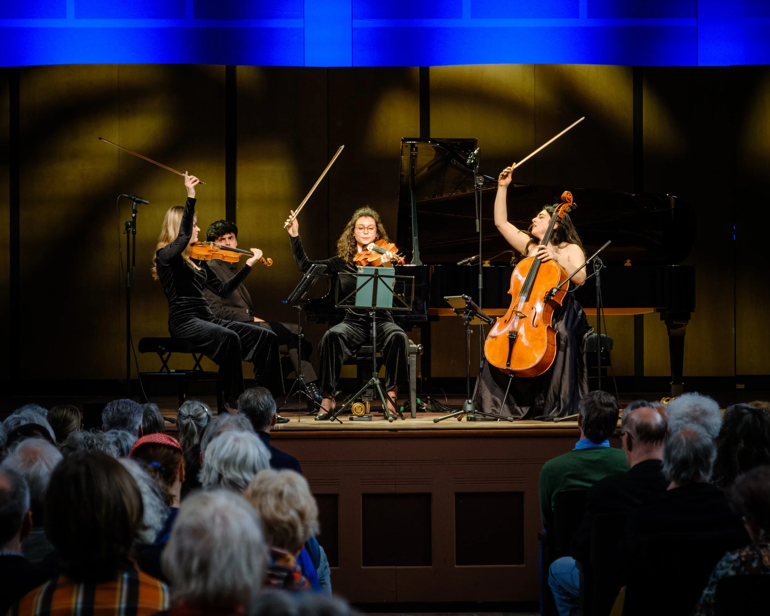 A classical string quartet performing on stage with audience watching.
