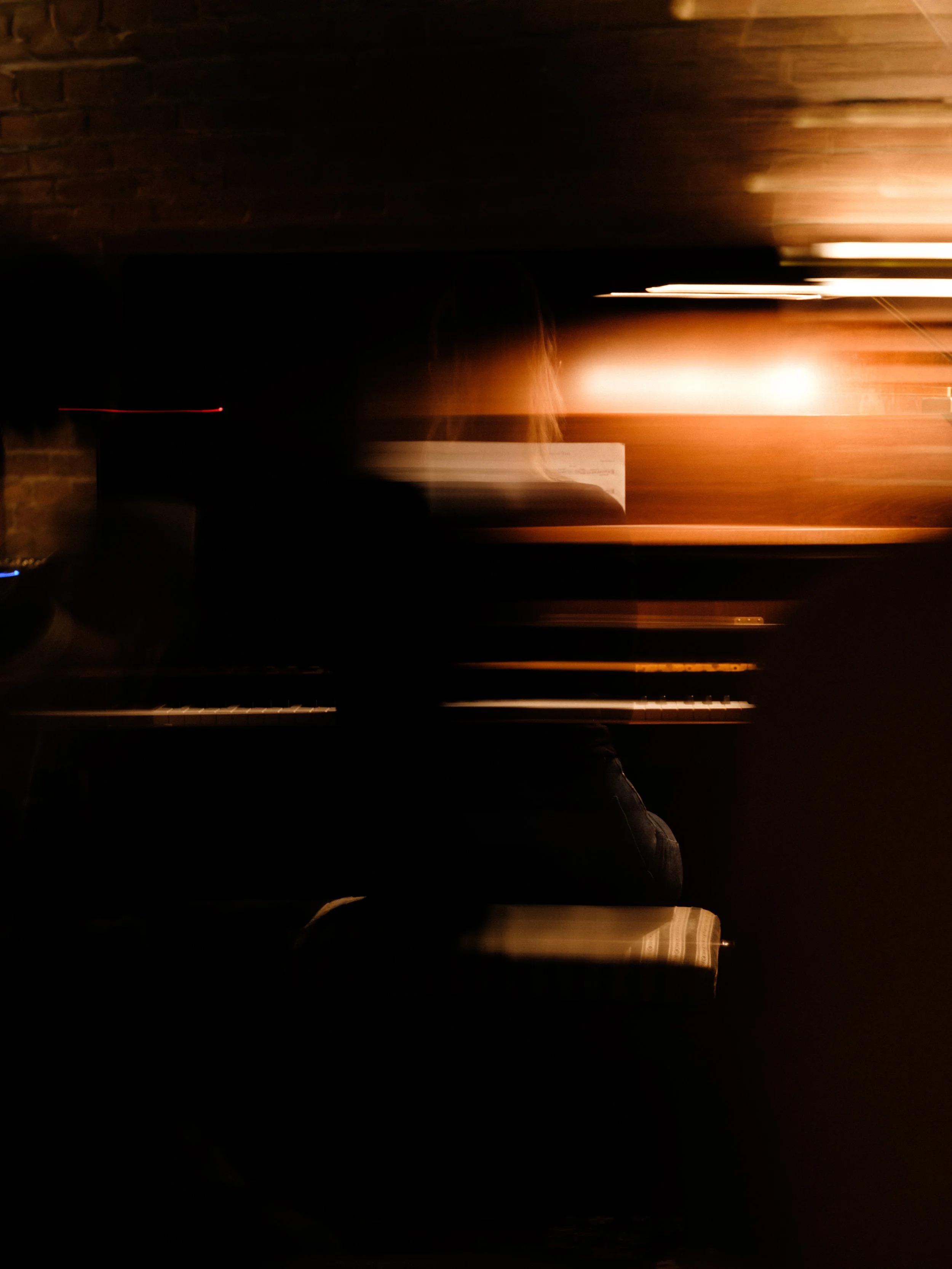 Dimly lit scene of a person playing piano with motion blur, dark background, and warm lighting.