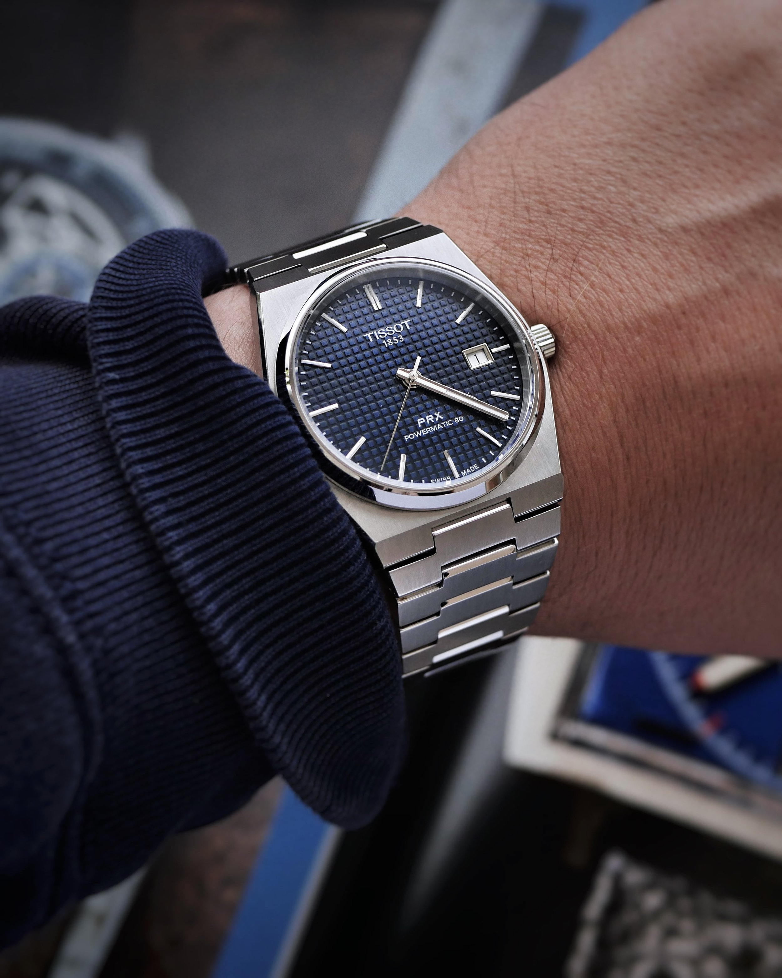 Close-up wrist shot of the Tissot PRX Powermatic 80 showing its blue waffle dial and steel bracelet