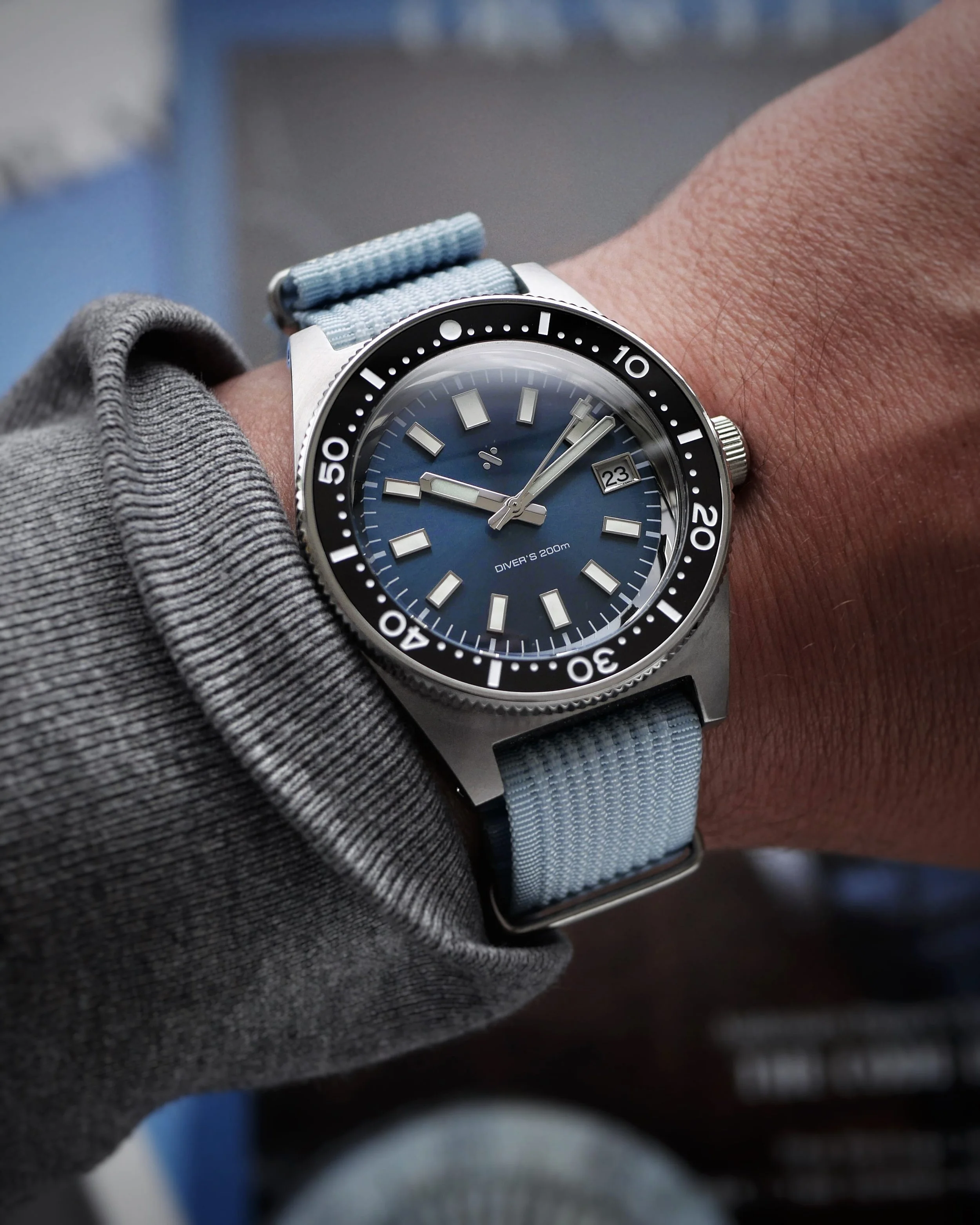 Namoki NMK07 blue sunburst dial and black bezel on the wrist with a pale blue woven strap.