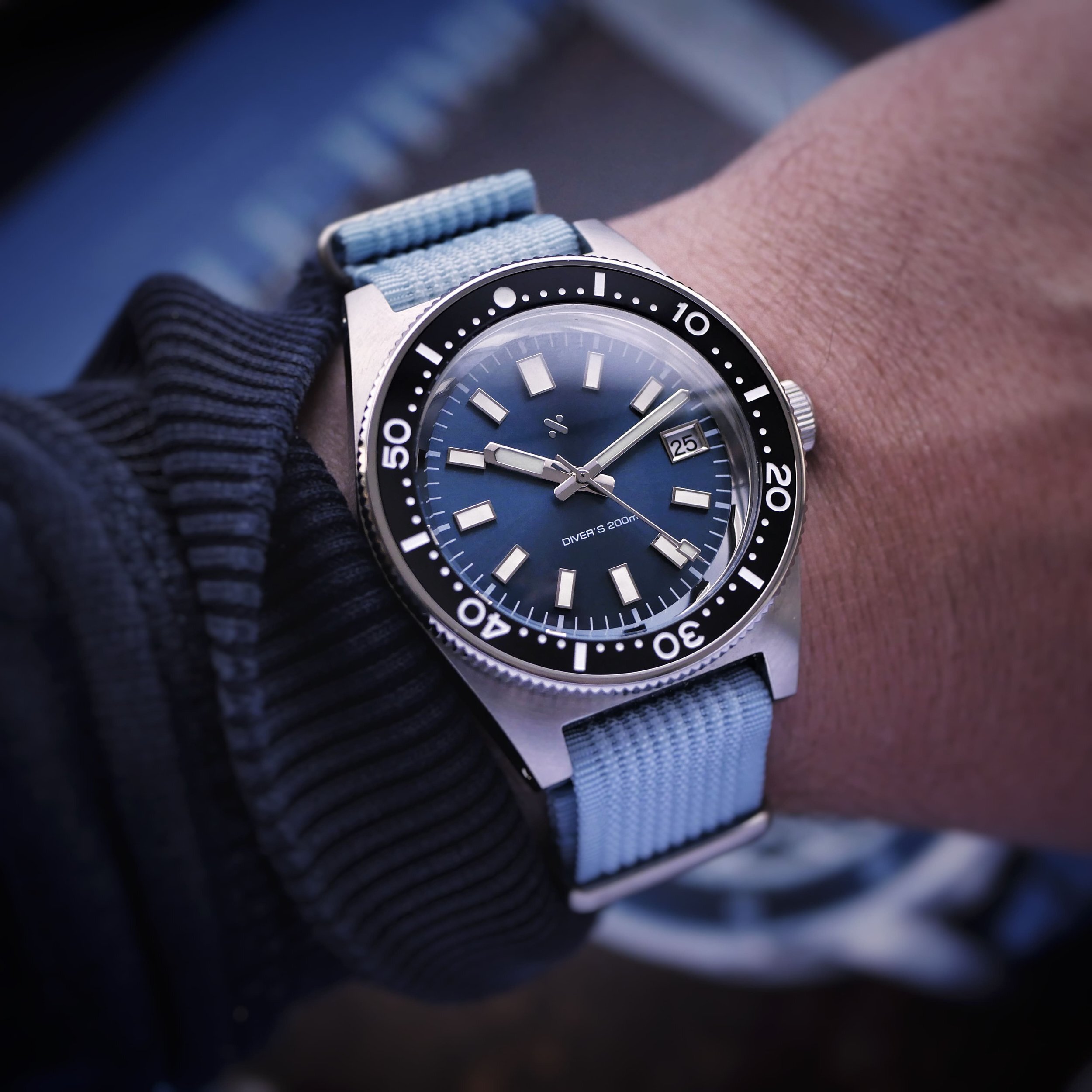 Close-up of the Namoki NMK07 on the wrist, showing its blue sunburst dial, date window and black bezel.