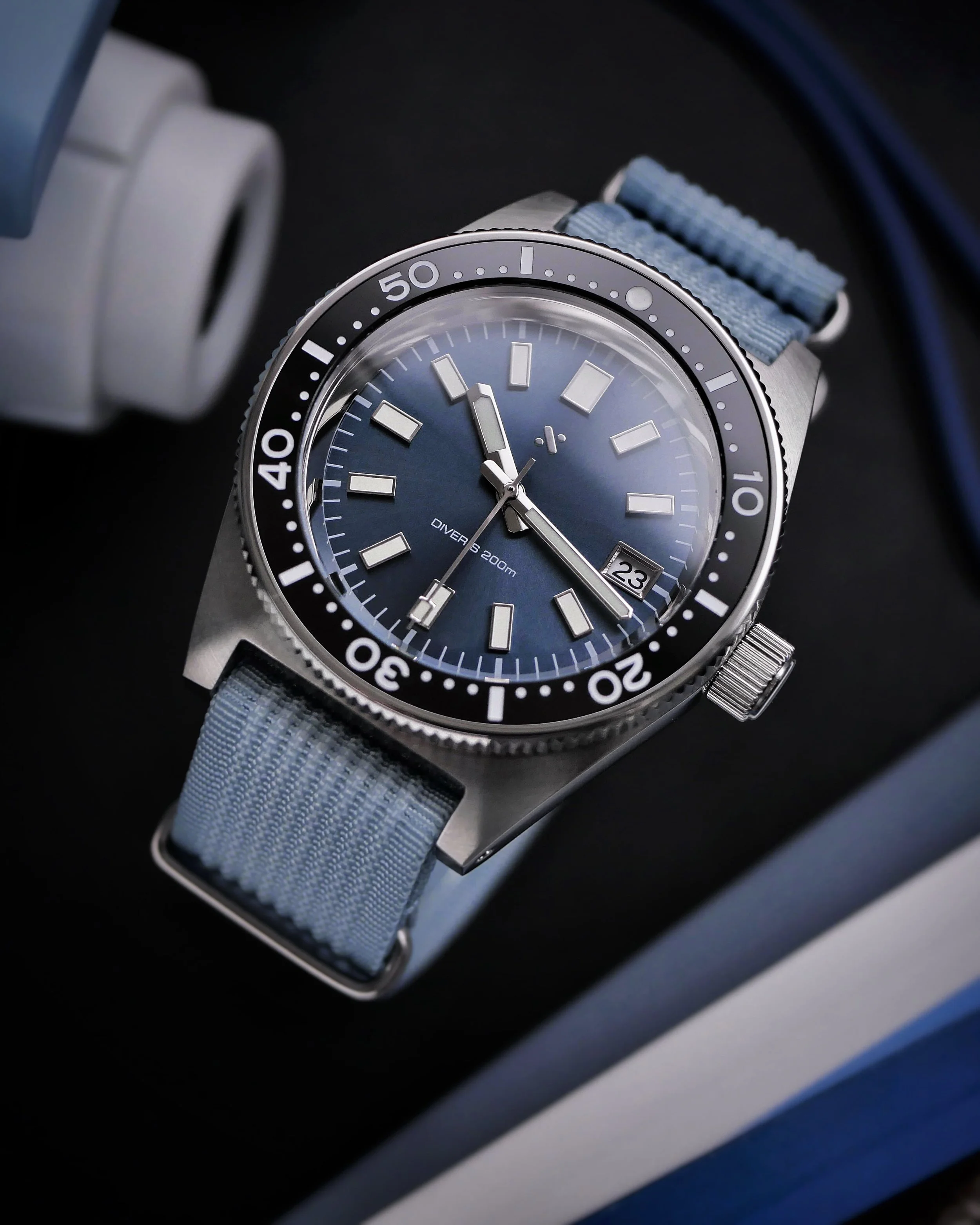 Angled view of the Namoki NMK07 showing its blue dial, domed crystal, crown and pale blue woven strap.