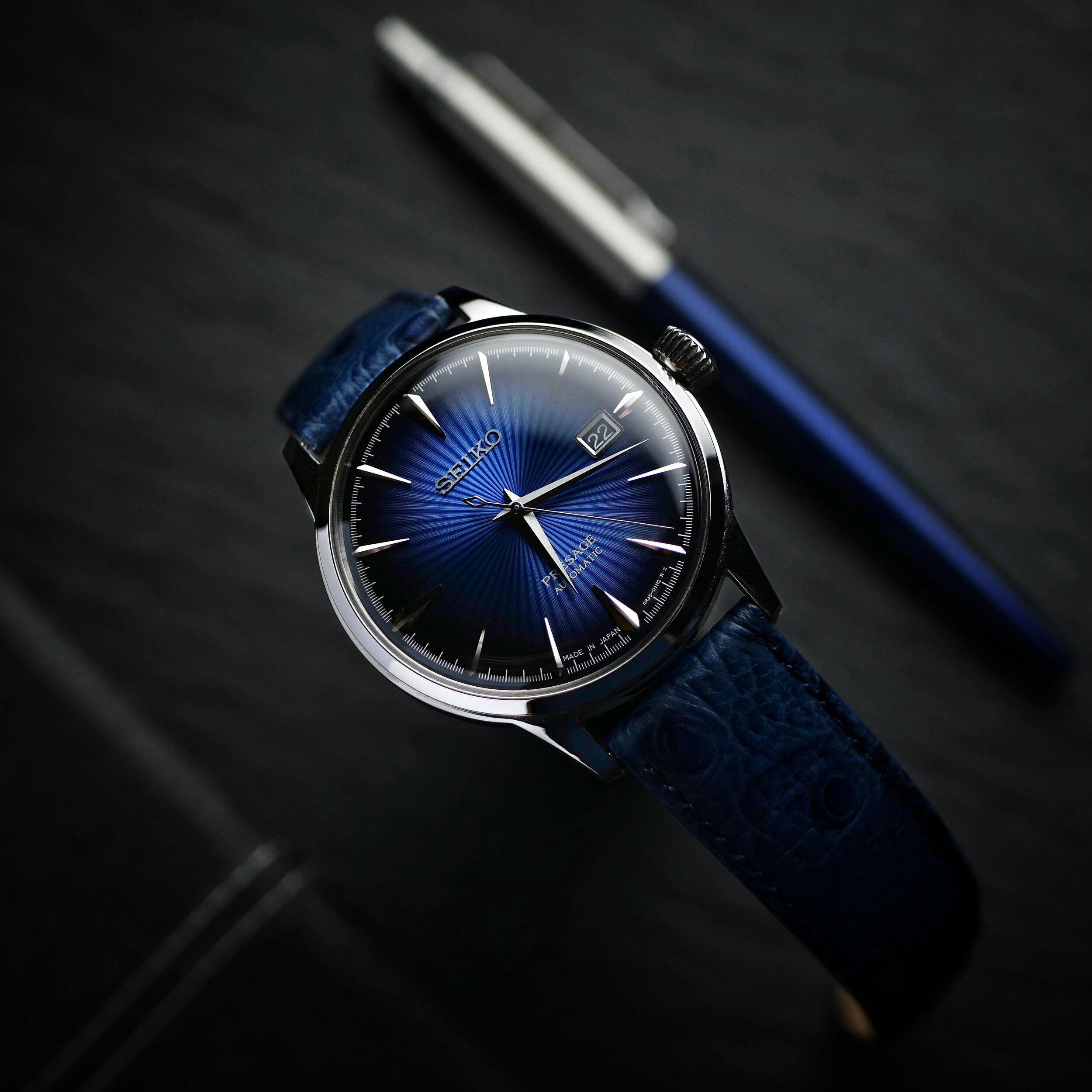 Seiko Presage Blue Moon SRPB41J1 showing its textured blue sunray dial on a matching blue leather strap, photographed beside a pen.