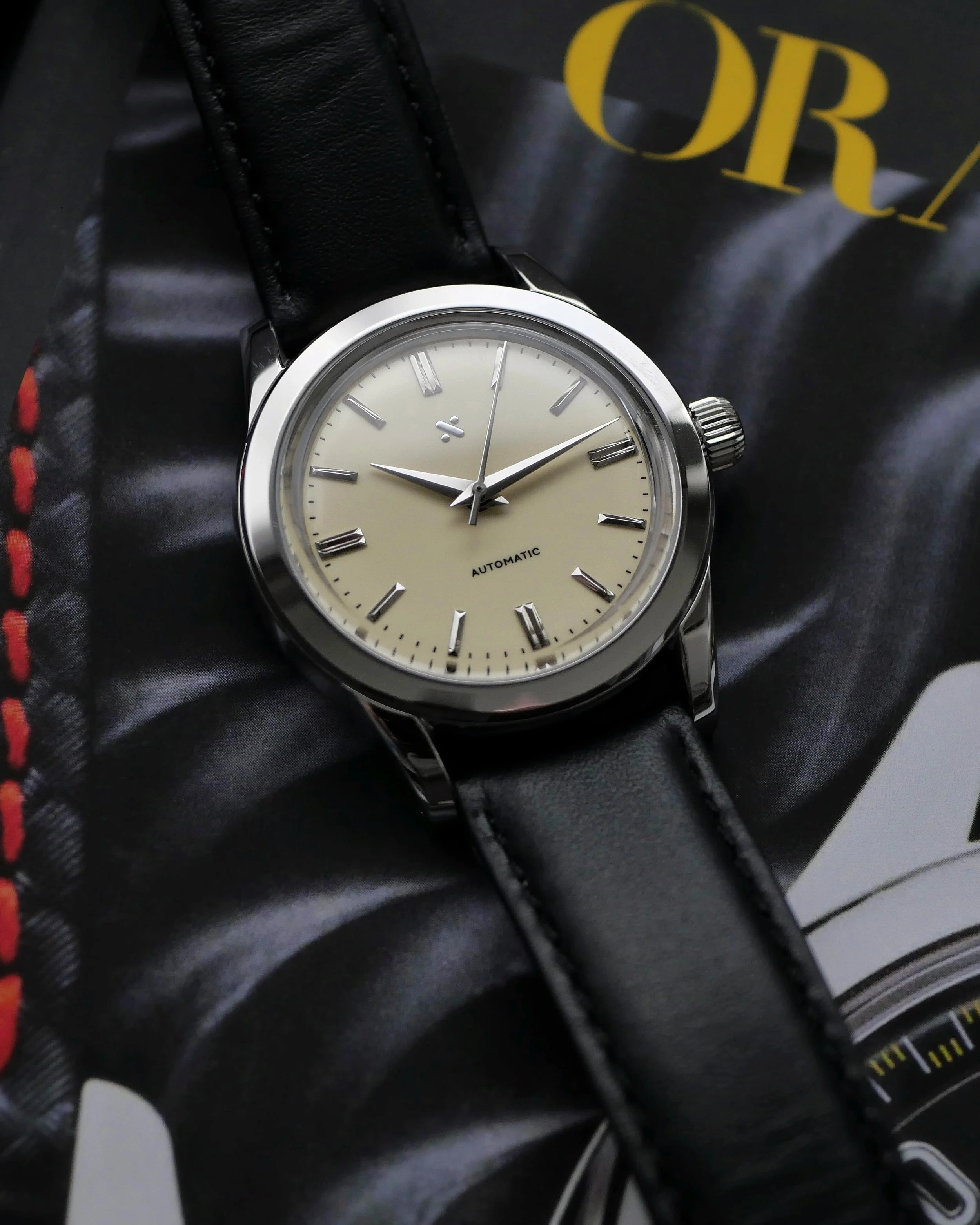 Close-up of the Namoki NMK15 cream-toned dial, pointed hands, polished hour markers and coin-edge crown