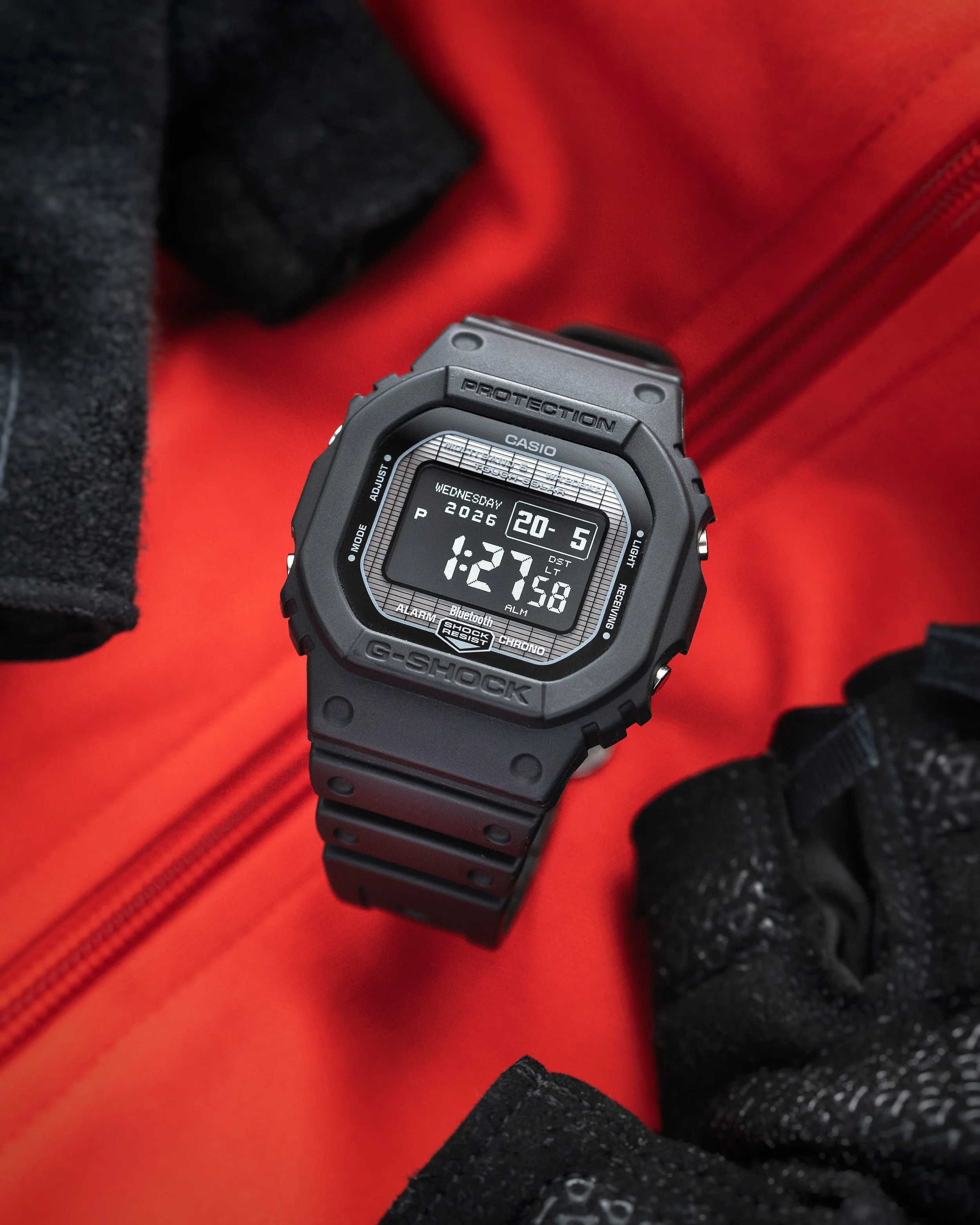 G-SHOCK GW-BX5600-1A1 negative display watch with black resin square case and clear MIP display on a red background