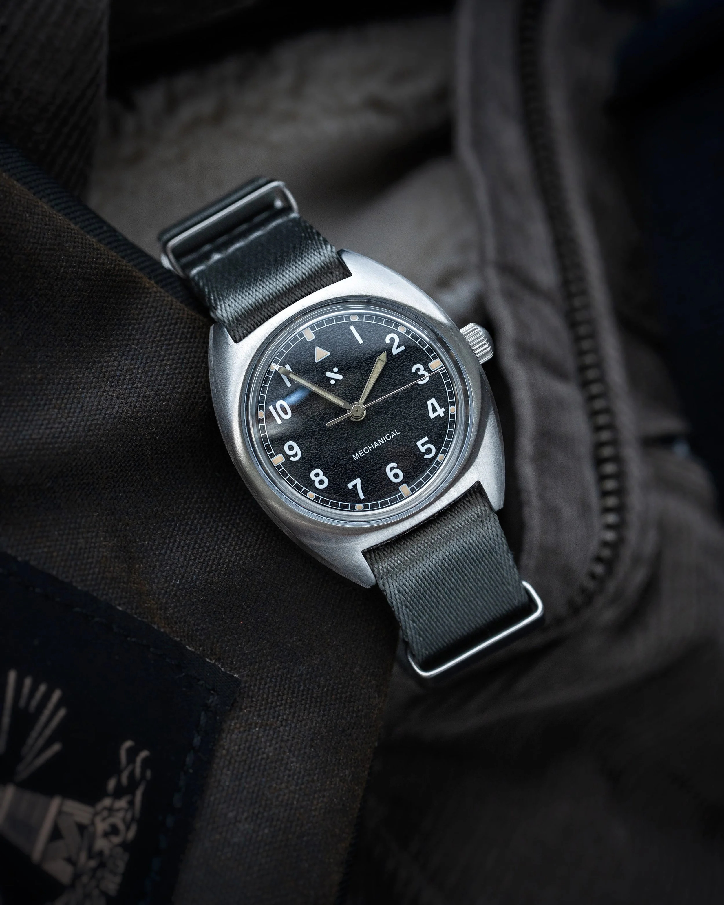 Angled shot of the Namoki Mods NMK21 pilot watch showing the satin steel case and black dial