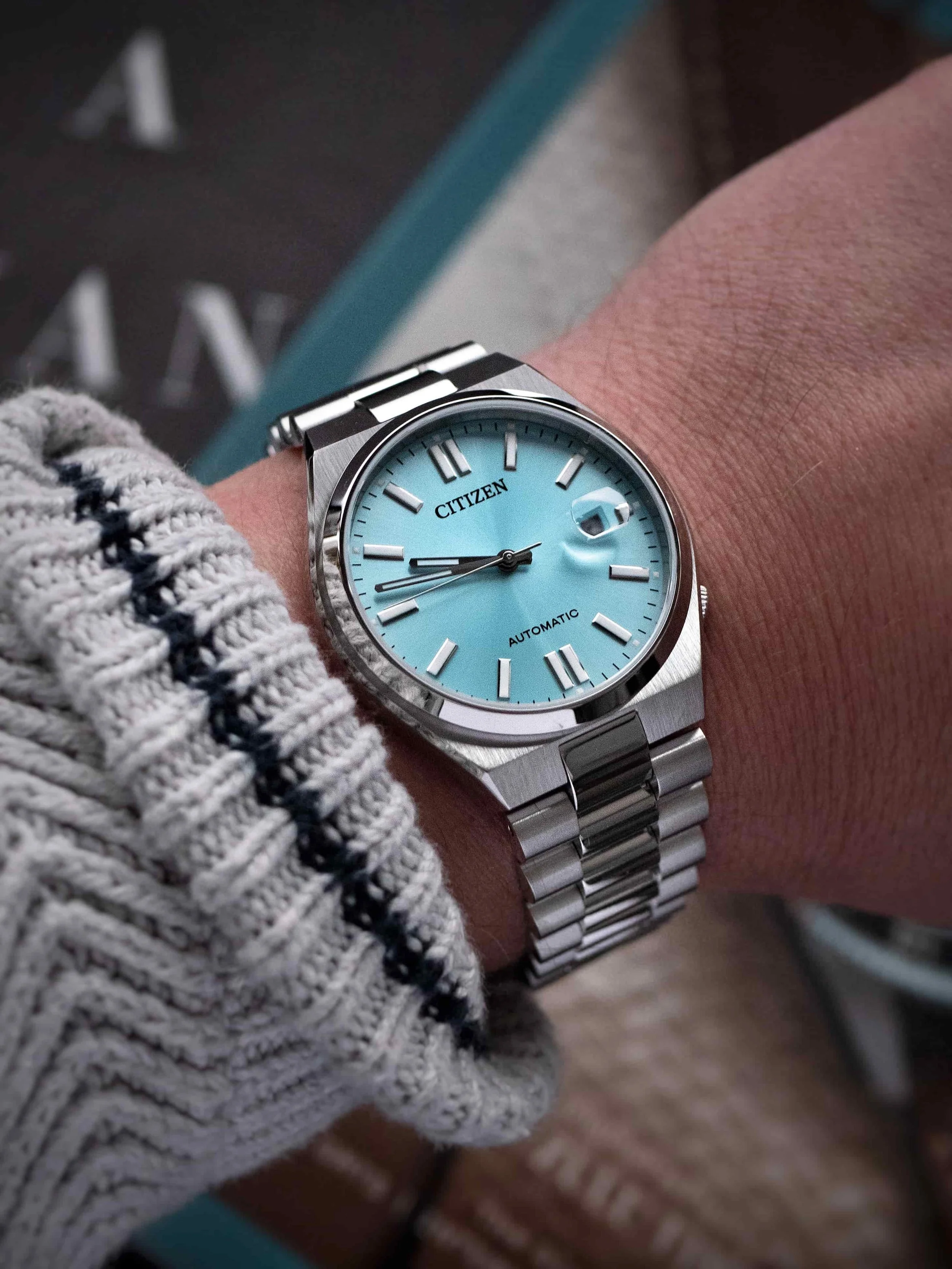 Citizen Tsuyosa automatic watch with turquoise blue dial on wrist, stainless-steel bracelet shown in natural light.
