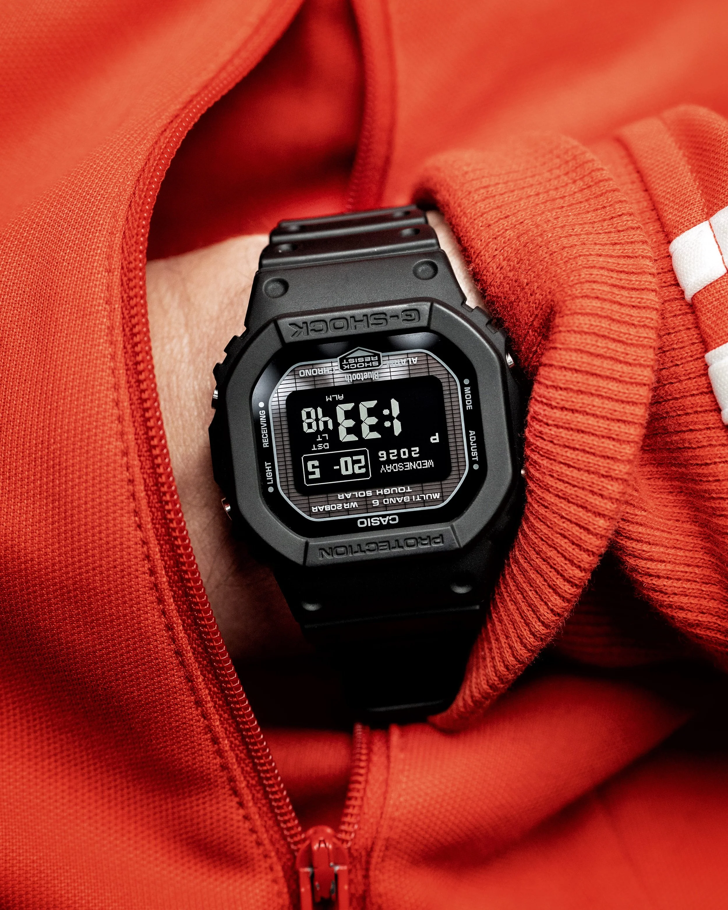 G-SHOCK GW-BX5600-1A1 worn on wrist with red clothing showing the compact black square case and negative MIP display