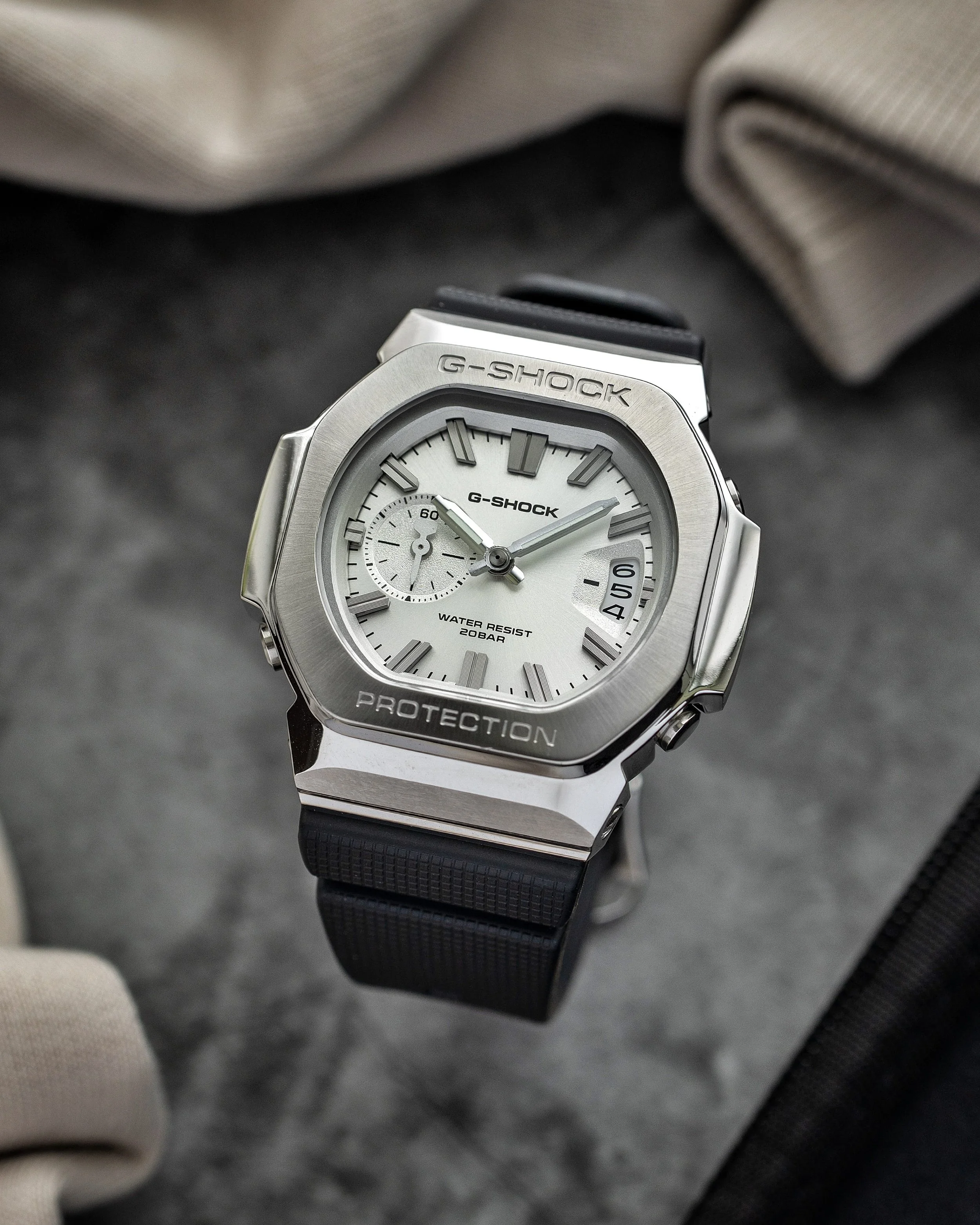 Casio G-SHOCK GMC-2500-1A8 CasioNaut with a brushed silver metal bezel, textured silver analogue dial, raised hour markers and black resin strap, photographed on a grey surface.