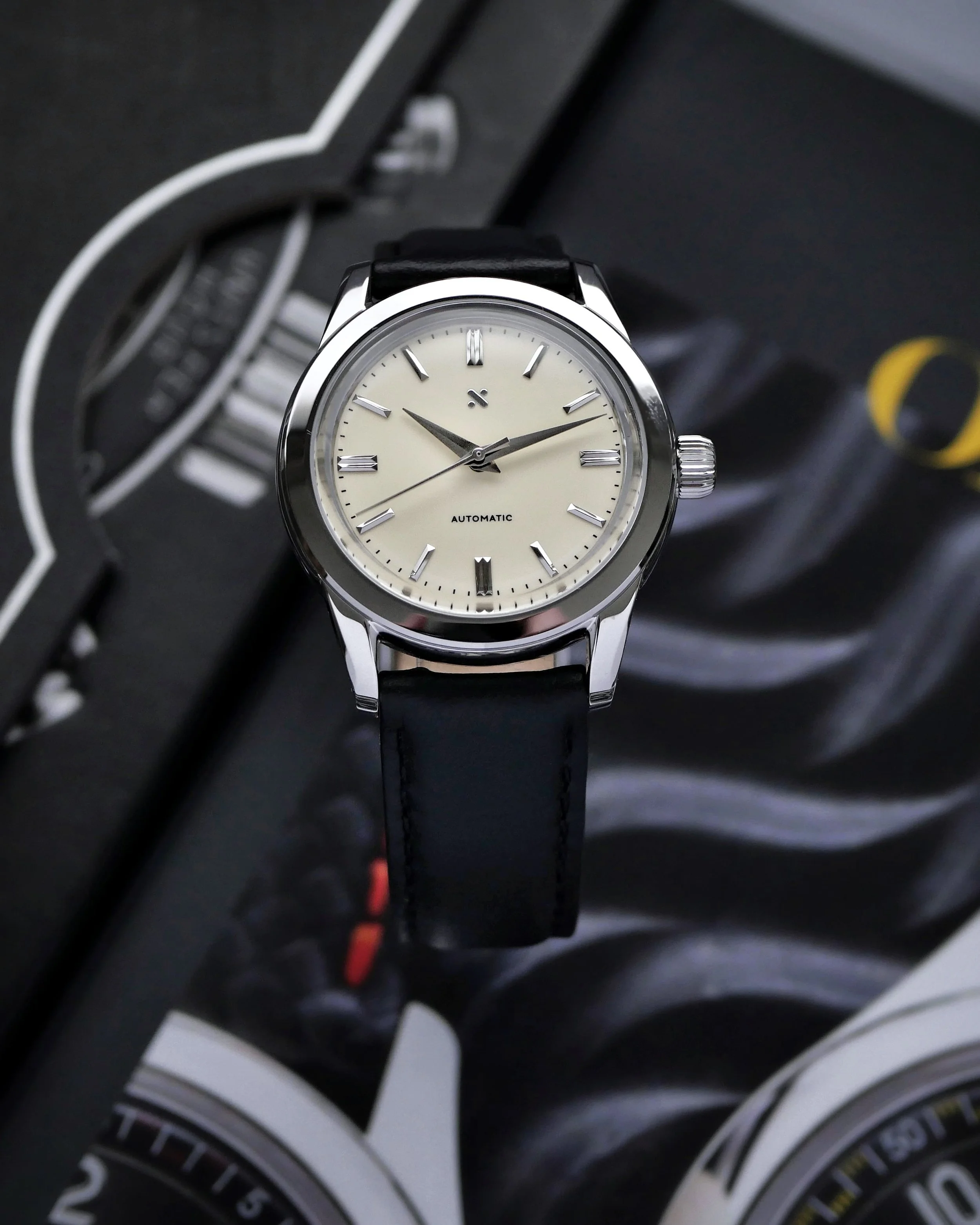 Namoki NMK15 GS Steel with cream-toned dial and black leather strap on an open watch magazine