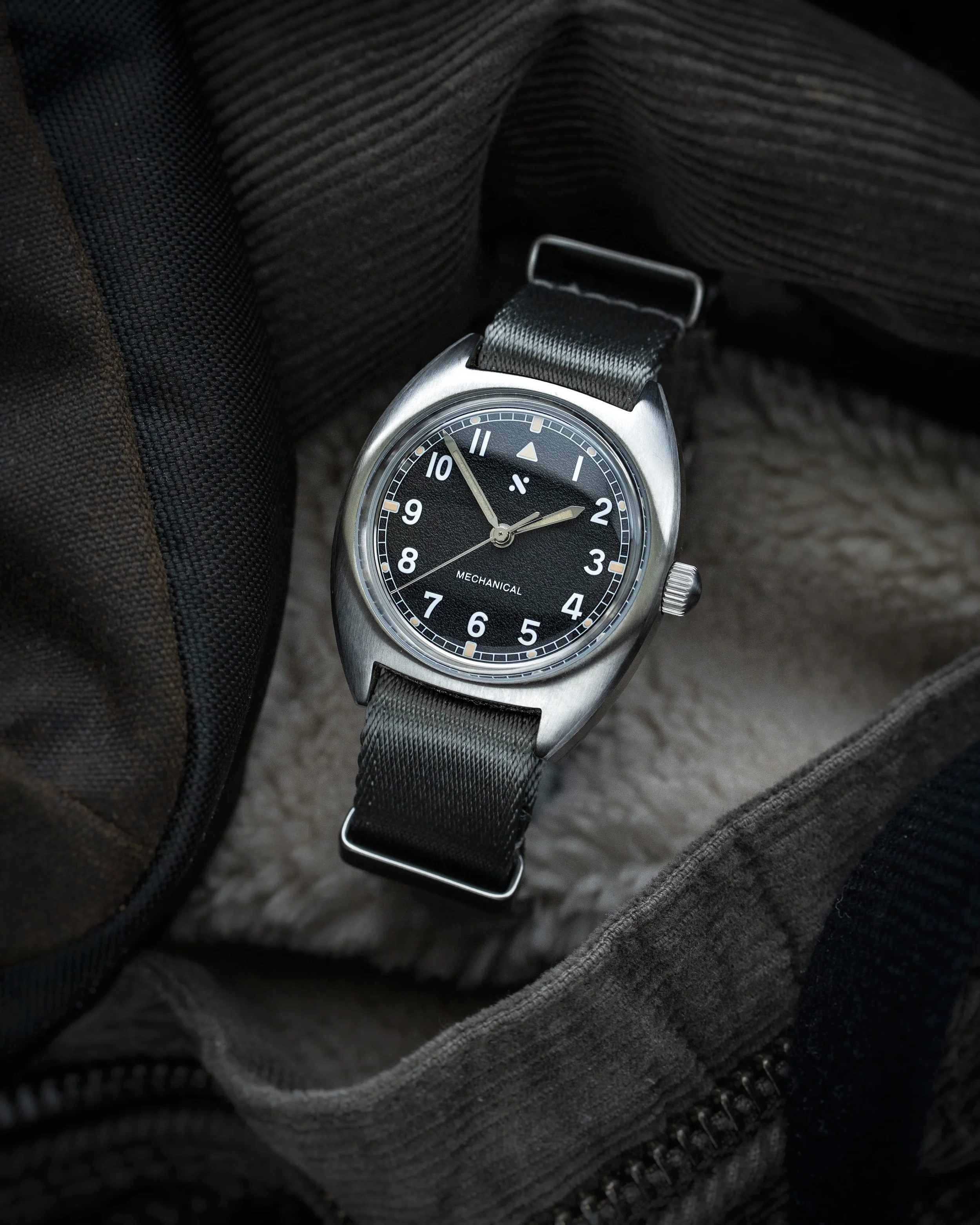 Angled view of the Namoki Mods NMK21 pilot watch showing the black dial and grey NATO strap