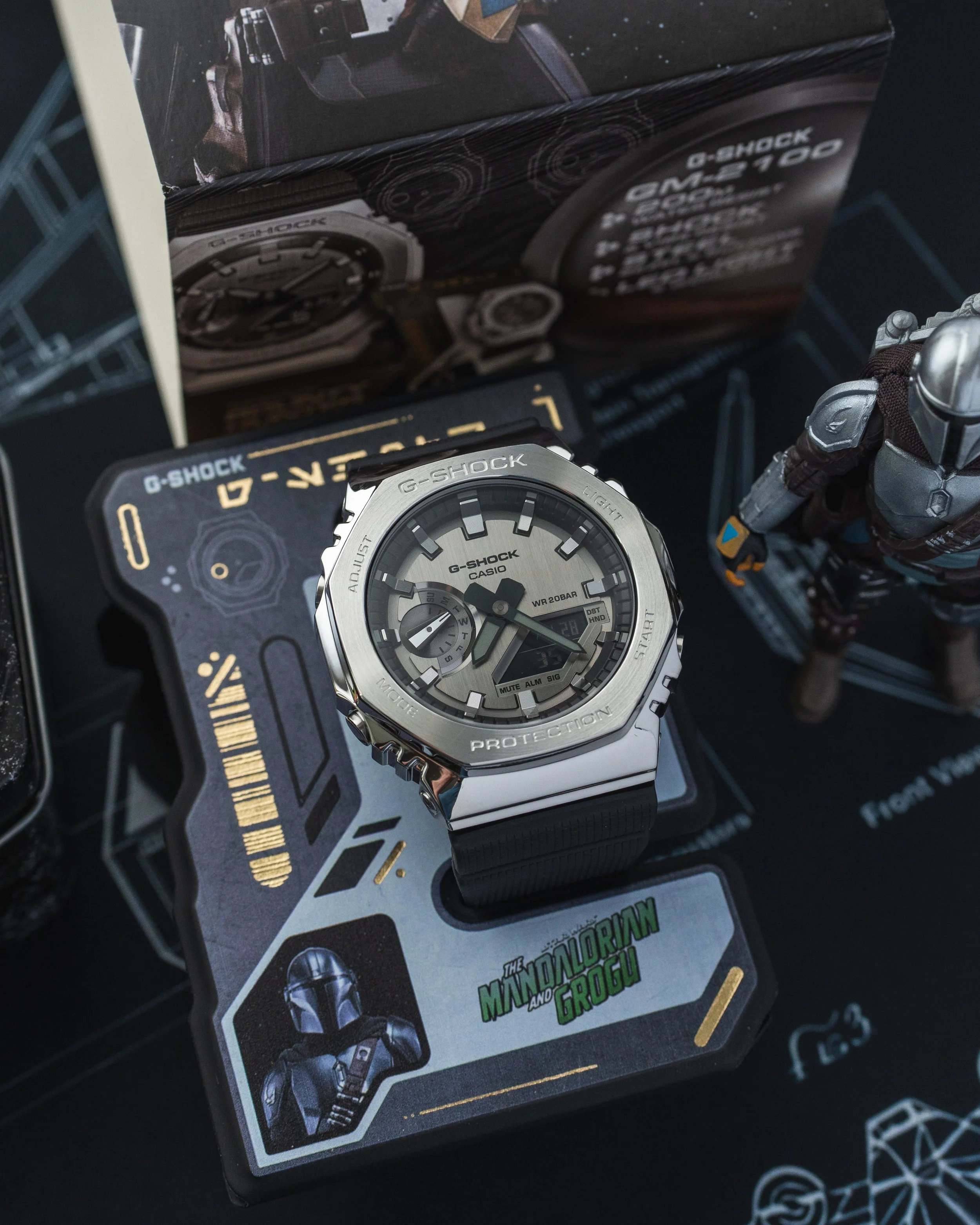 G-SHOCK GM-2100 Mandalorian watch with Beskar-inspired steel finish displayed on its Bounty Hunter ID stand
