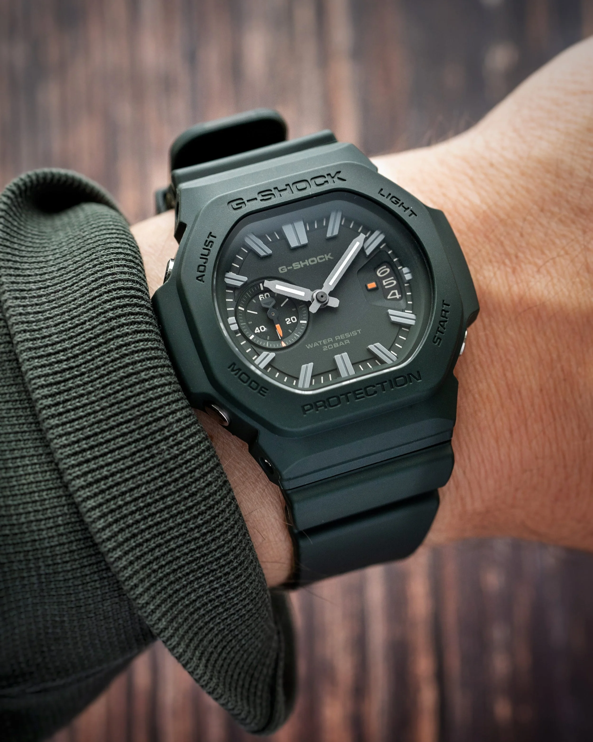 Casio G-SHOCK GAC-2500-3A CasioNaut worn on the wrist, showing its dark green resin case and strap, matching analogue dial, raised silver-tone markers and subtle orange accents.