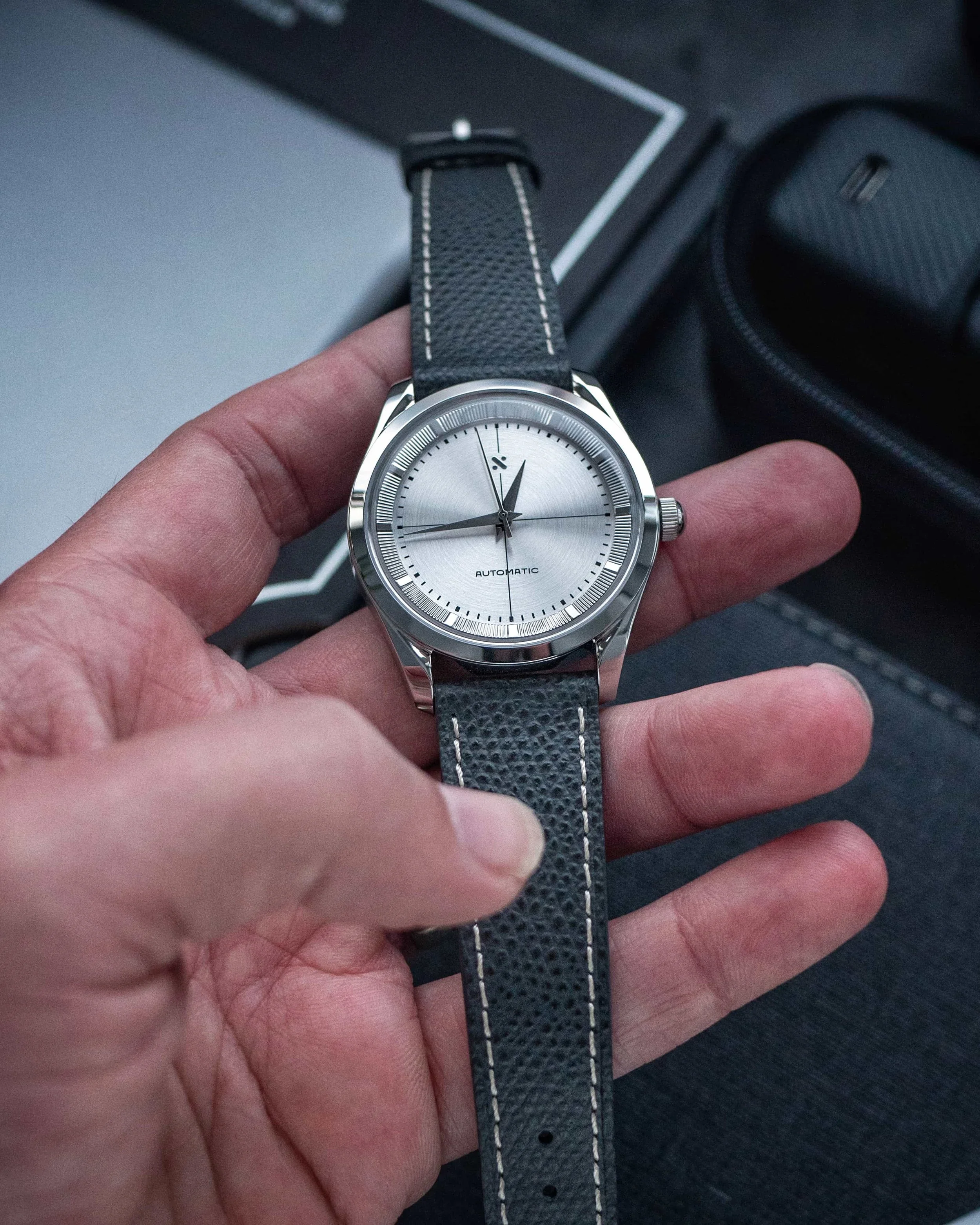 Namoki NMK953 build held in the hand, showing the grey leather strap and pale stitching
