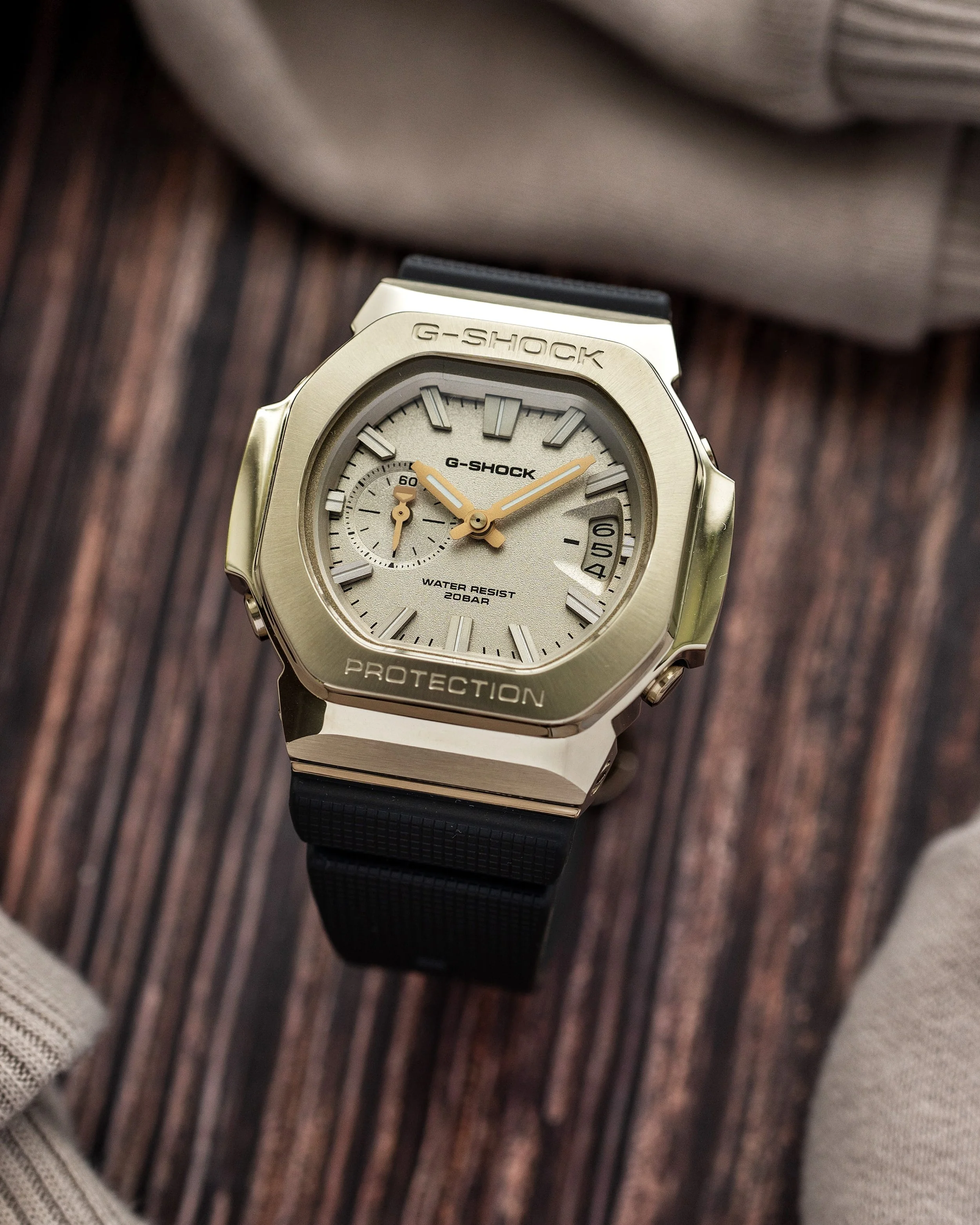 Casio G-SHOCK GMC-2500G-9A CasioNaut featuring a brushed champagne-gold metal bezel, textured gold dial, raised hour markers and black resin strap, photographed on a wooden surface.