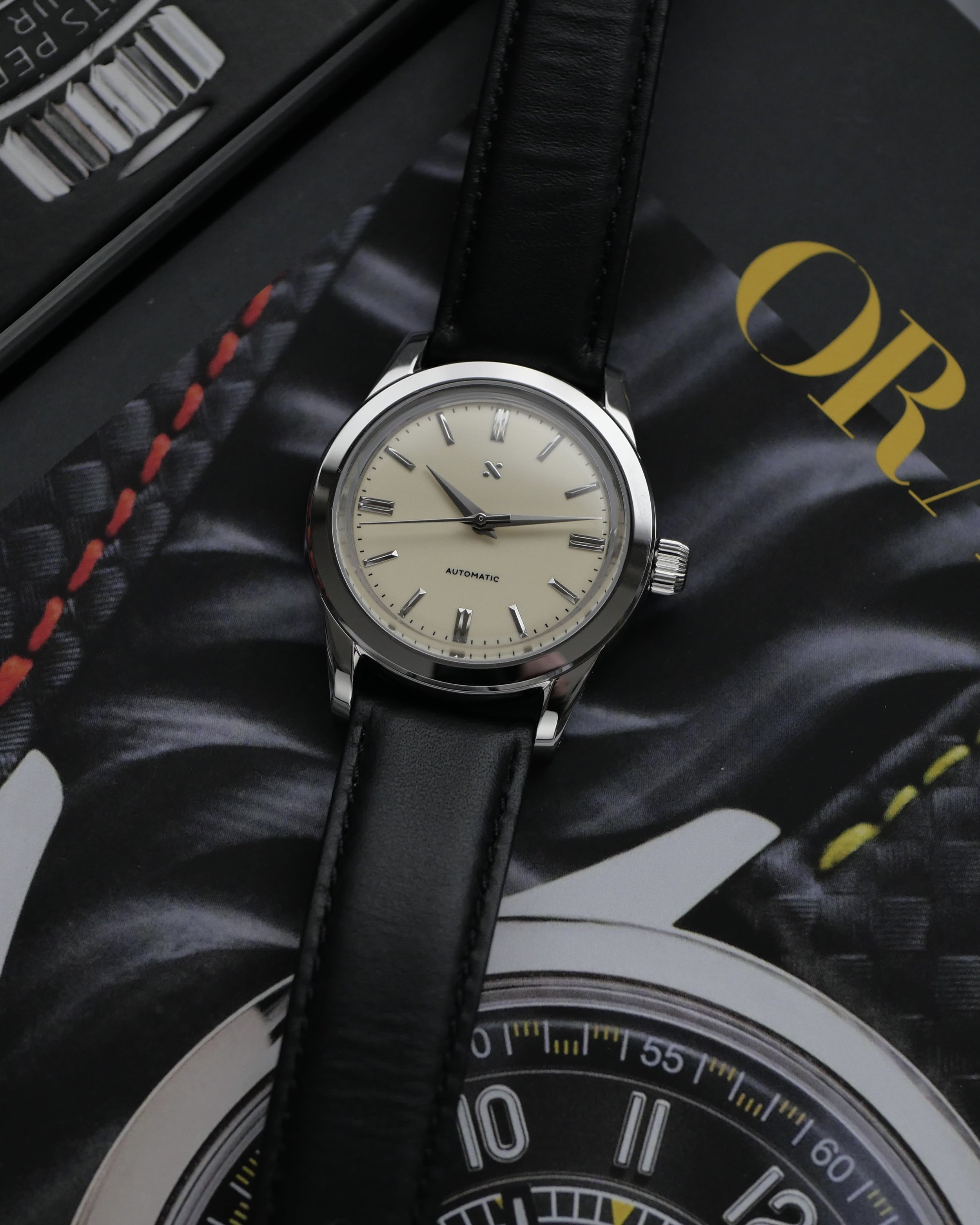 Namoki NMK15 arranged diagonally on a watch magazine, showing its polished case and black leather strap