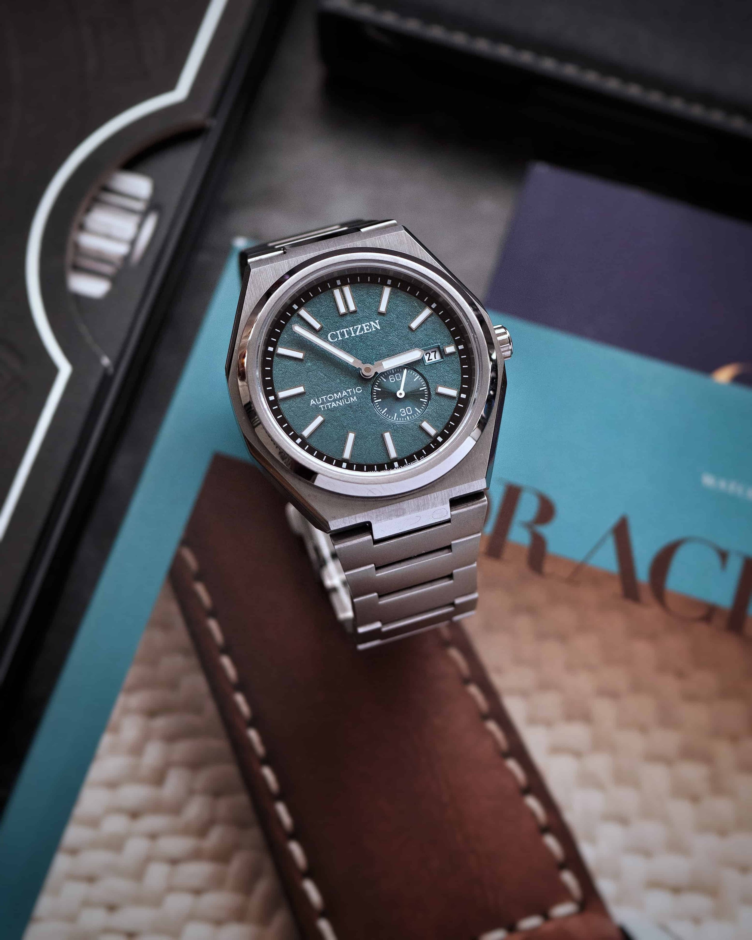 Citizen Zenshin NJ0180-80X Super Titanium displayed in a flatlay scene, showing the green textured dial and titanium bracelet.