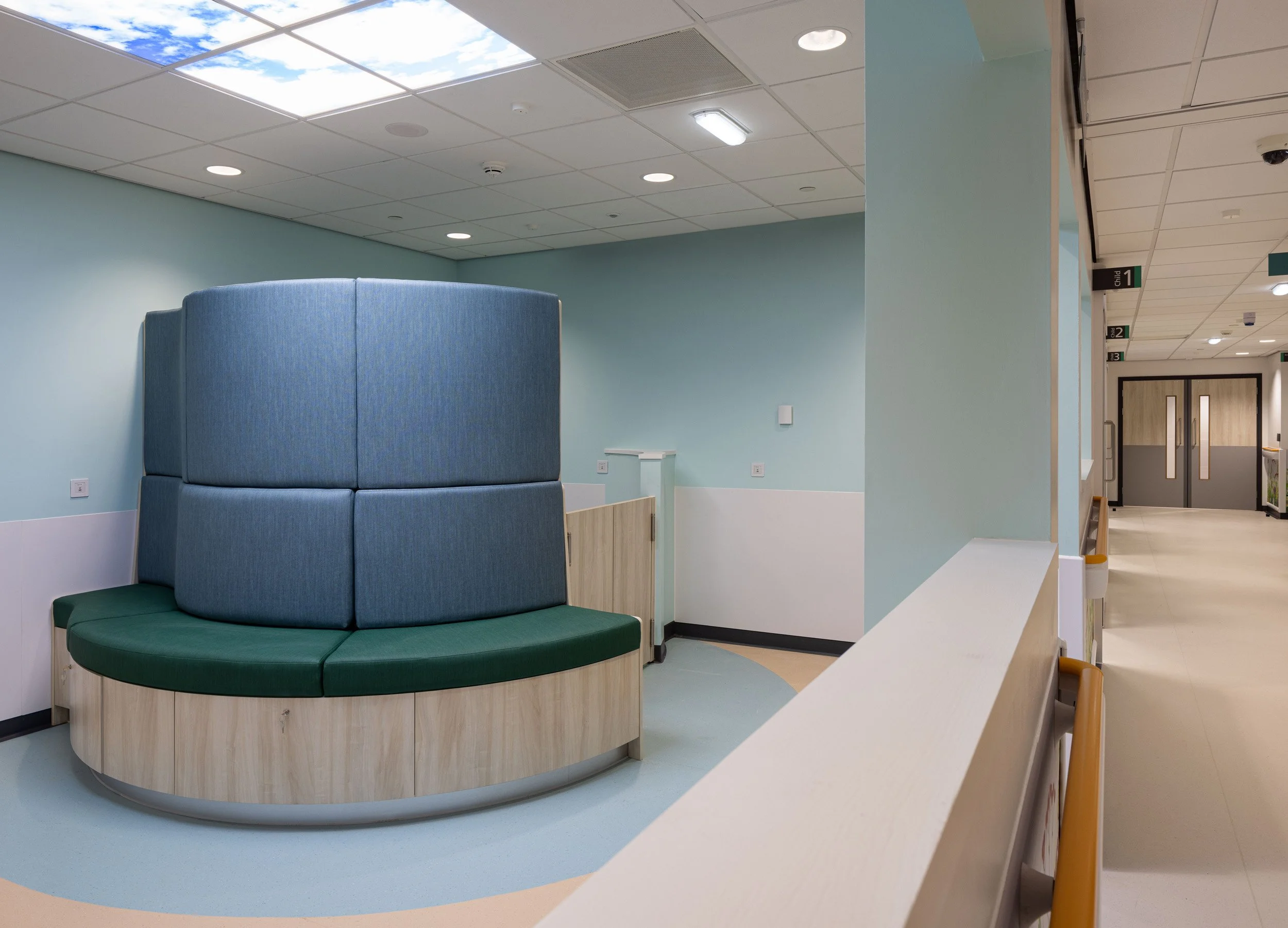 Empty hospital waiting area with teal and green seating and blue walls.