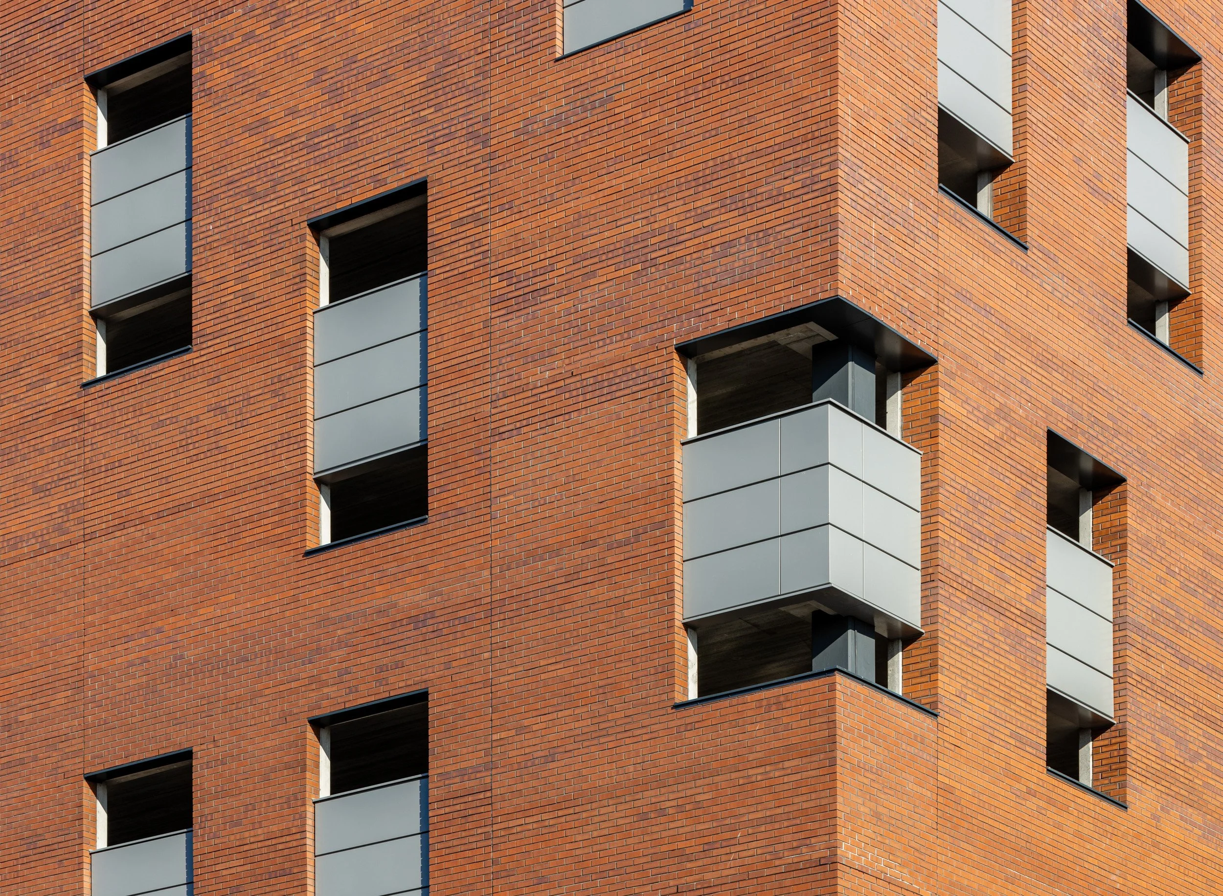 Close-up of a modern brick apartment building with open balconies and rectangular windows.
