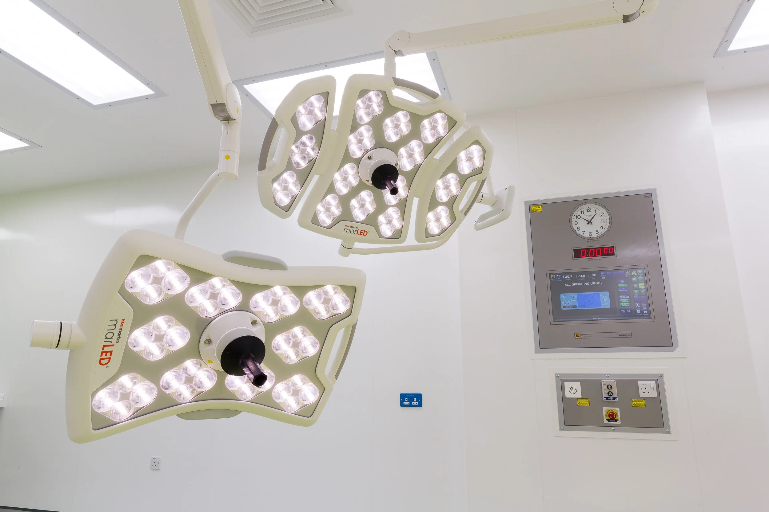 Two surgical ceiling lights in an operating room with control panels and a clock on the wall.