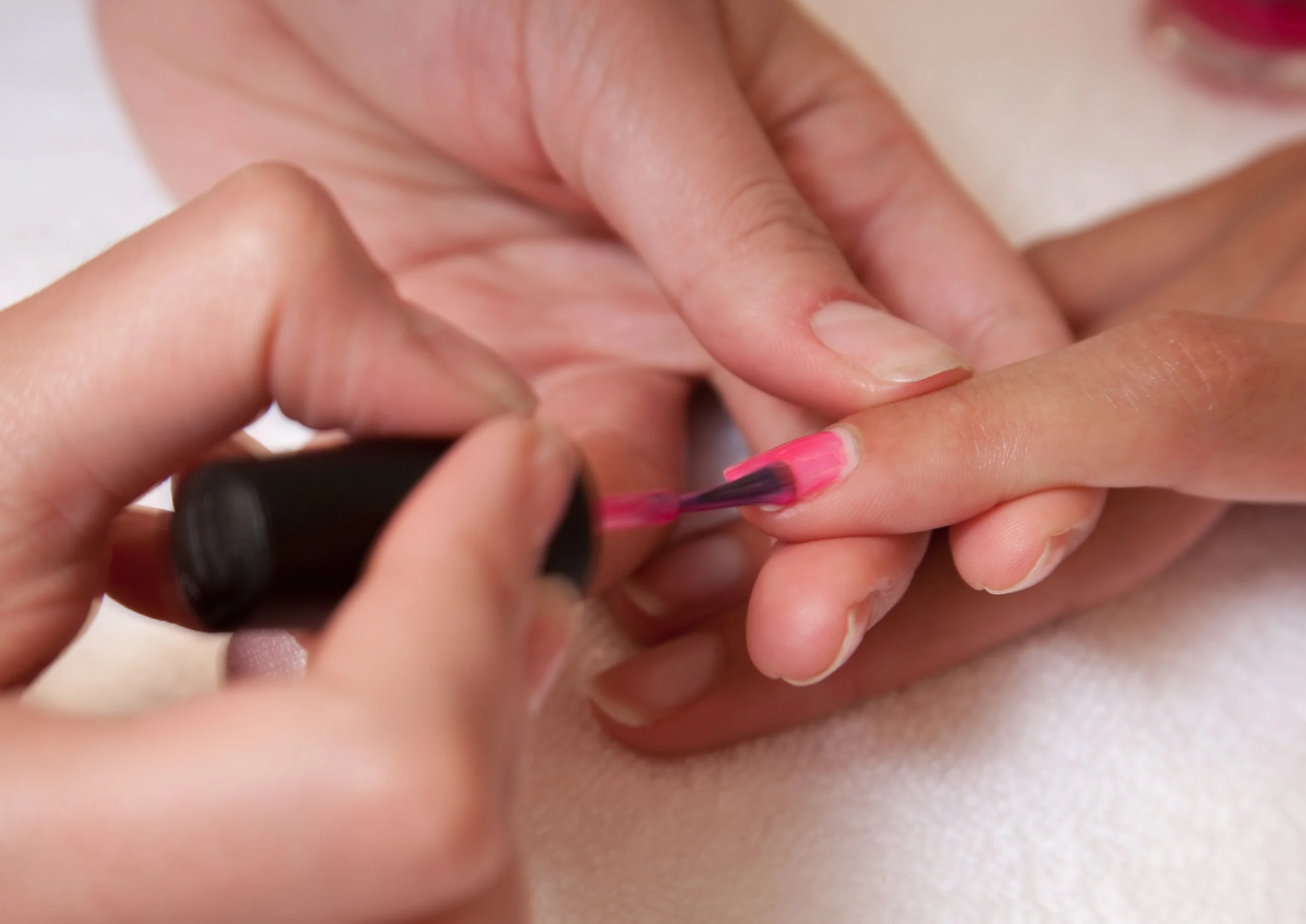 Close-up of a person applying pink nail polish to another person's fingernail.