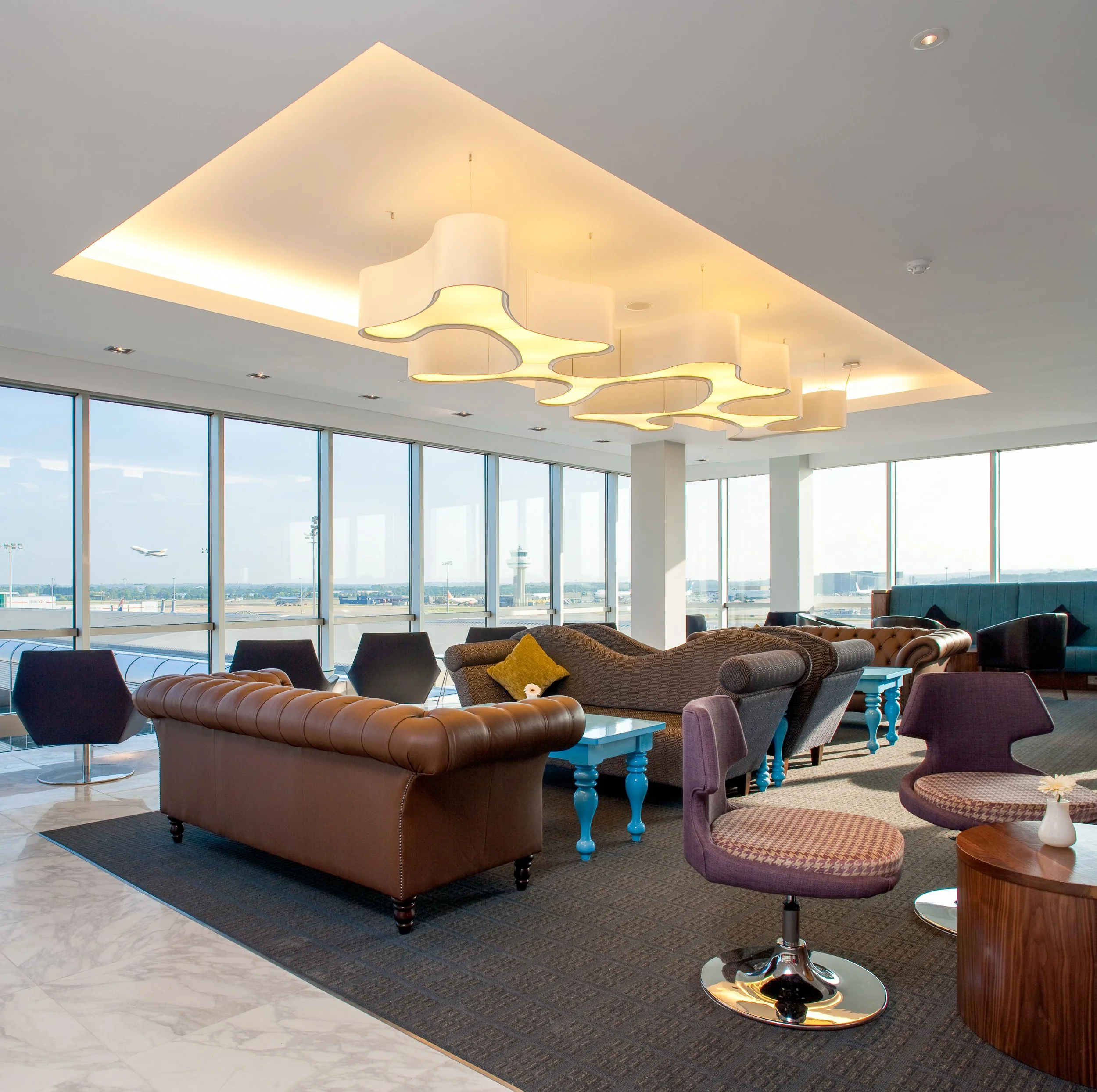 Modern airport lounge with large windows, contemporary furniture, and ceiling light fixture.