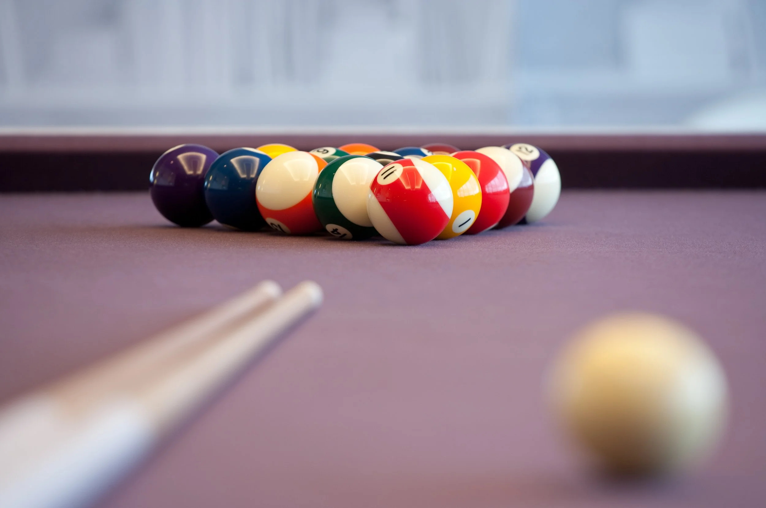 Pool table with billiard balls arranged in a triangle and a cue stick in the foreground.