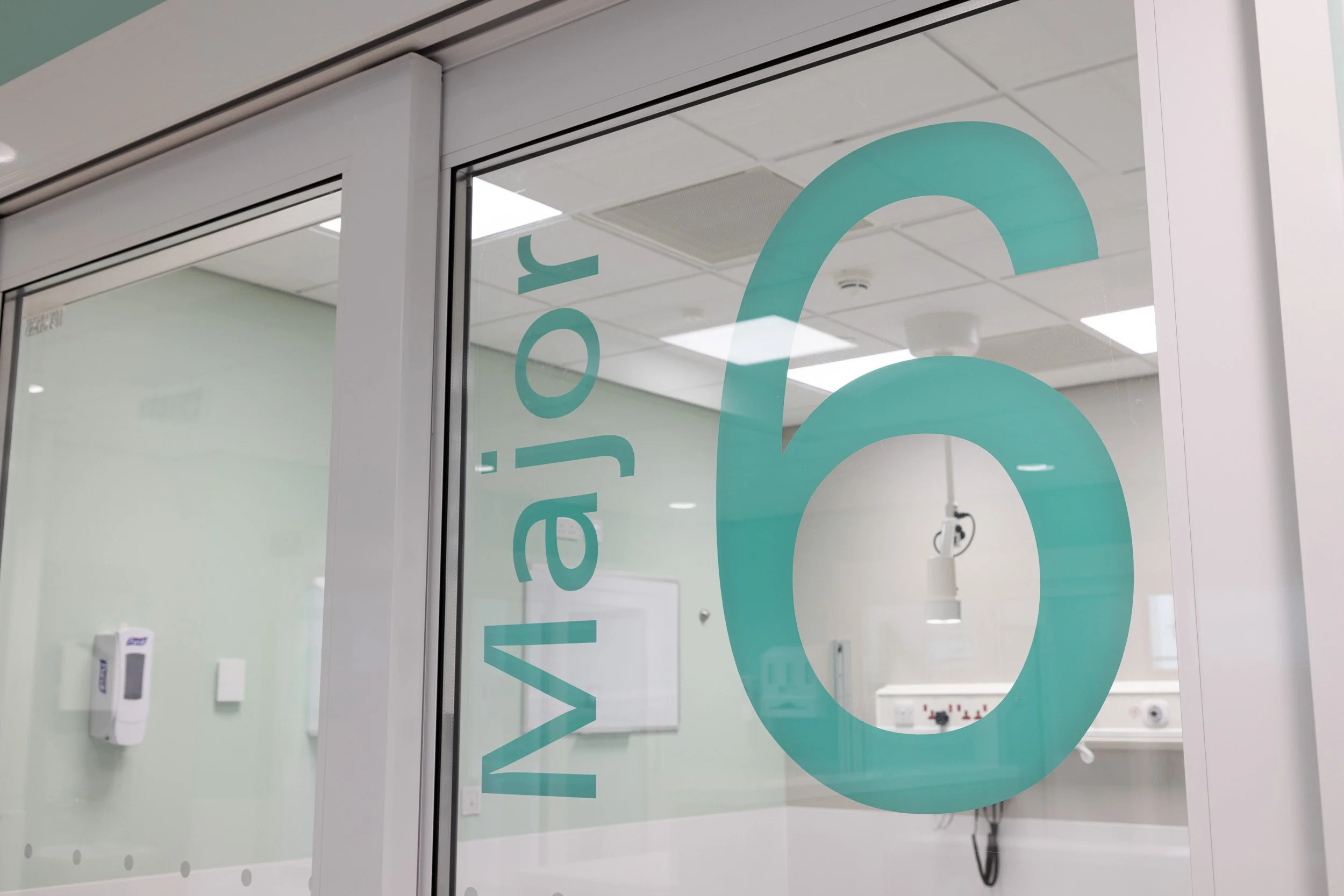 Hospital room with the number 6 on a glass door that has the words 'Vailo J.' written vertically.