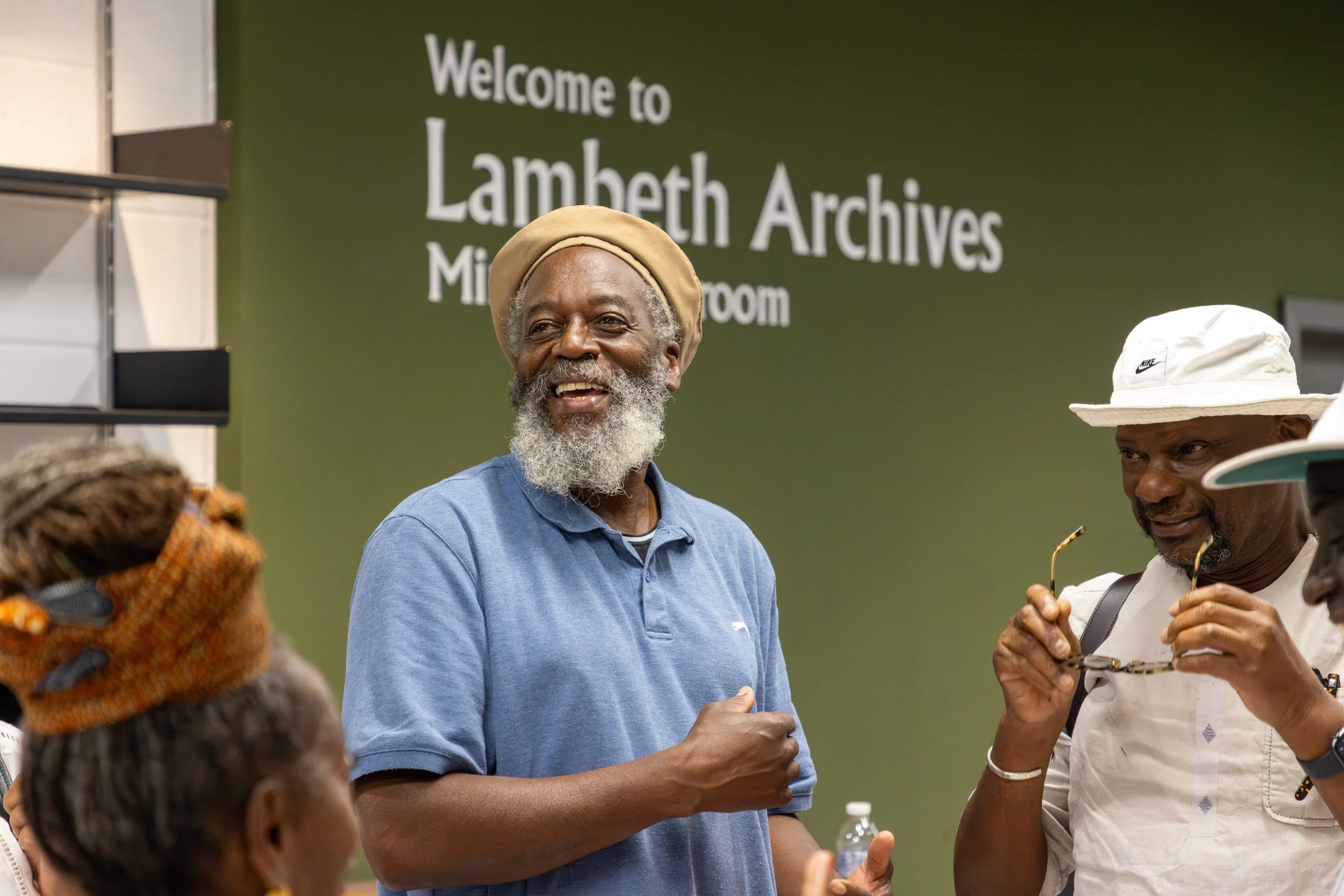 A group of people standing and talking in front of a green wall that says 'Welcome to Lambeth Archives'.