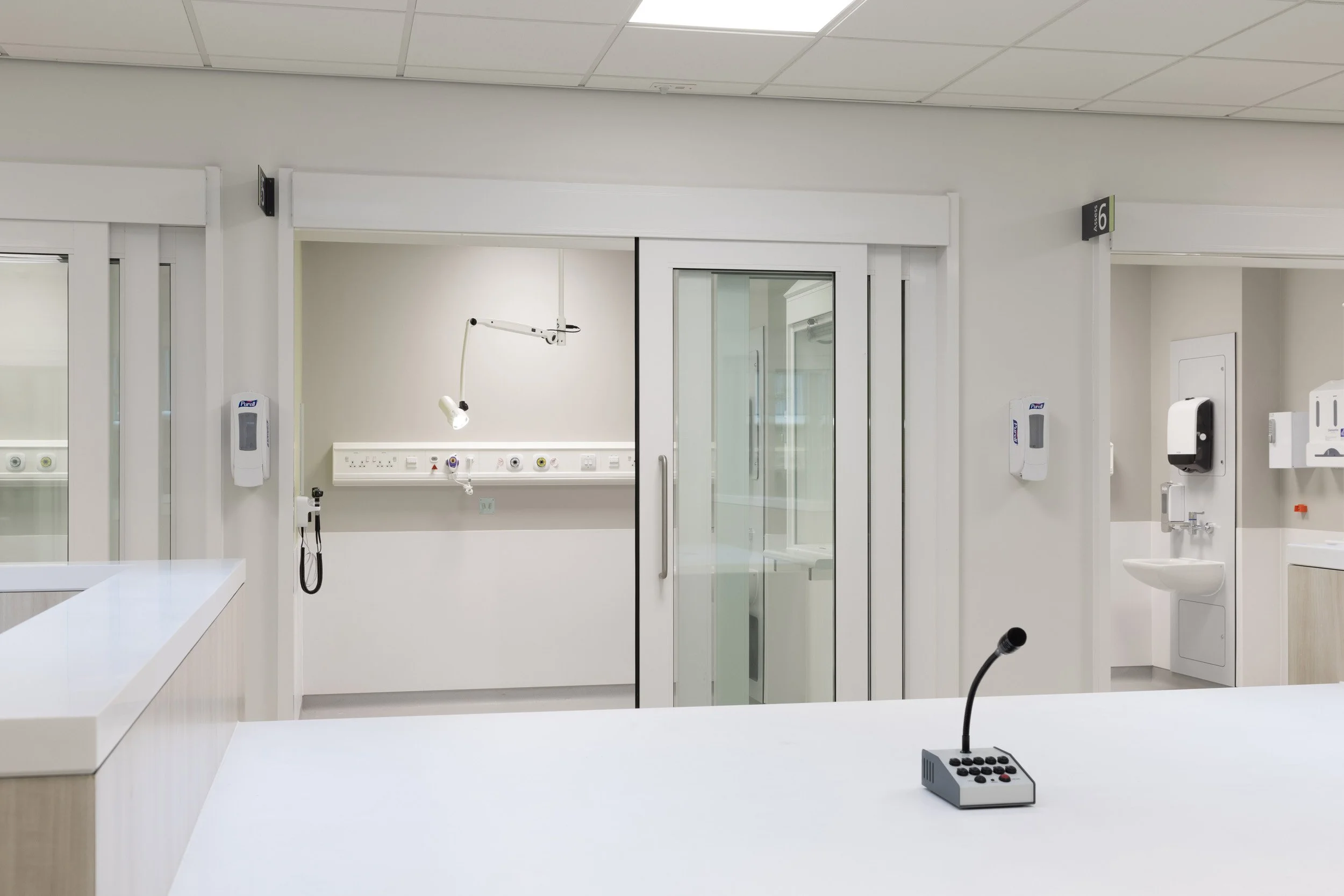 Empty hospital room with a privacy glass door, medical equipment, and a microphone on the desk.