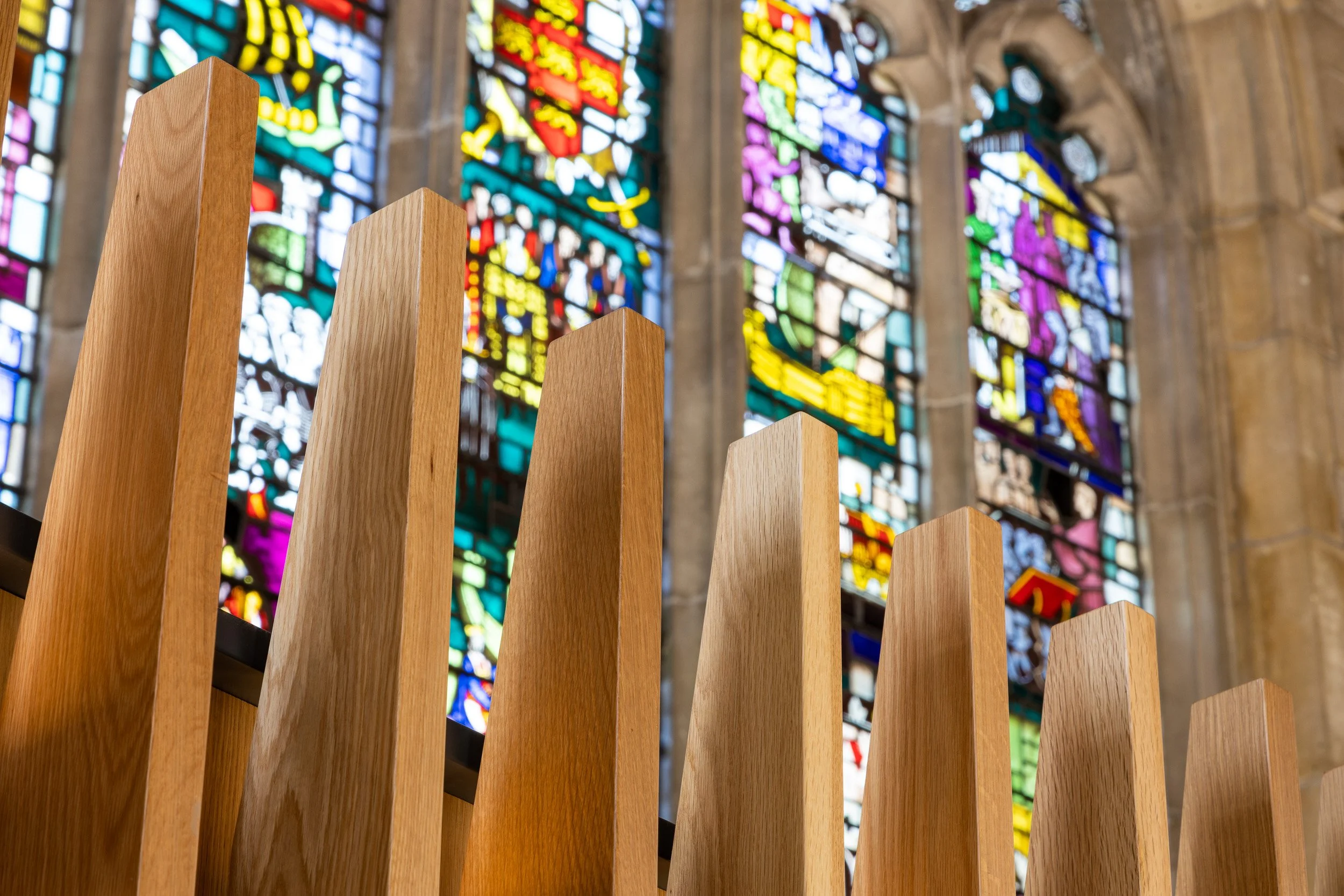 Wooden church organ pipes with stained glass windows in the background.
