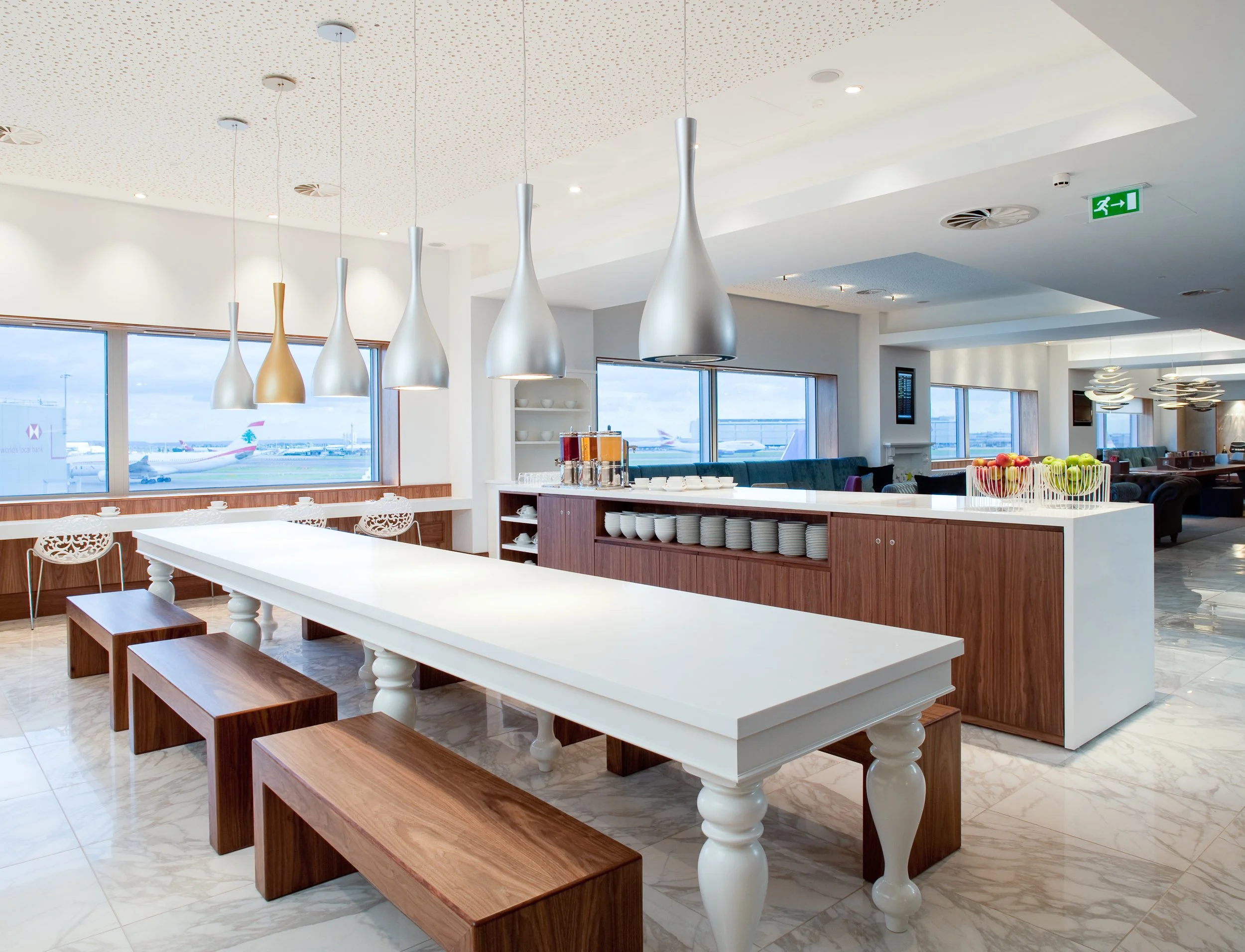 Airport lounge with large windows, seating area, and a refreshment counter with fruit bowls