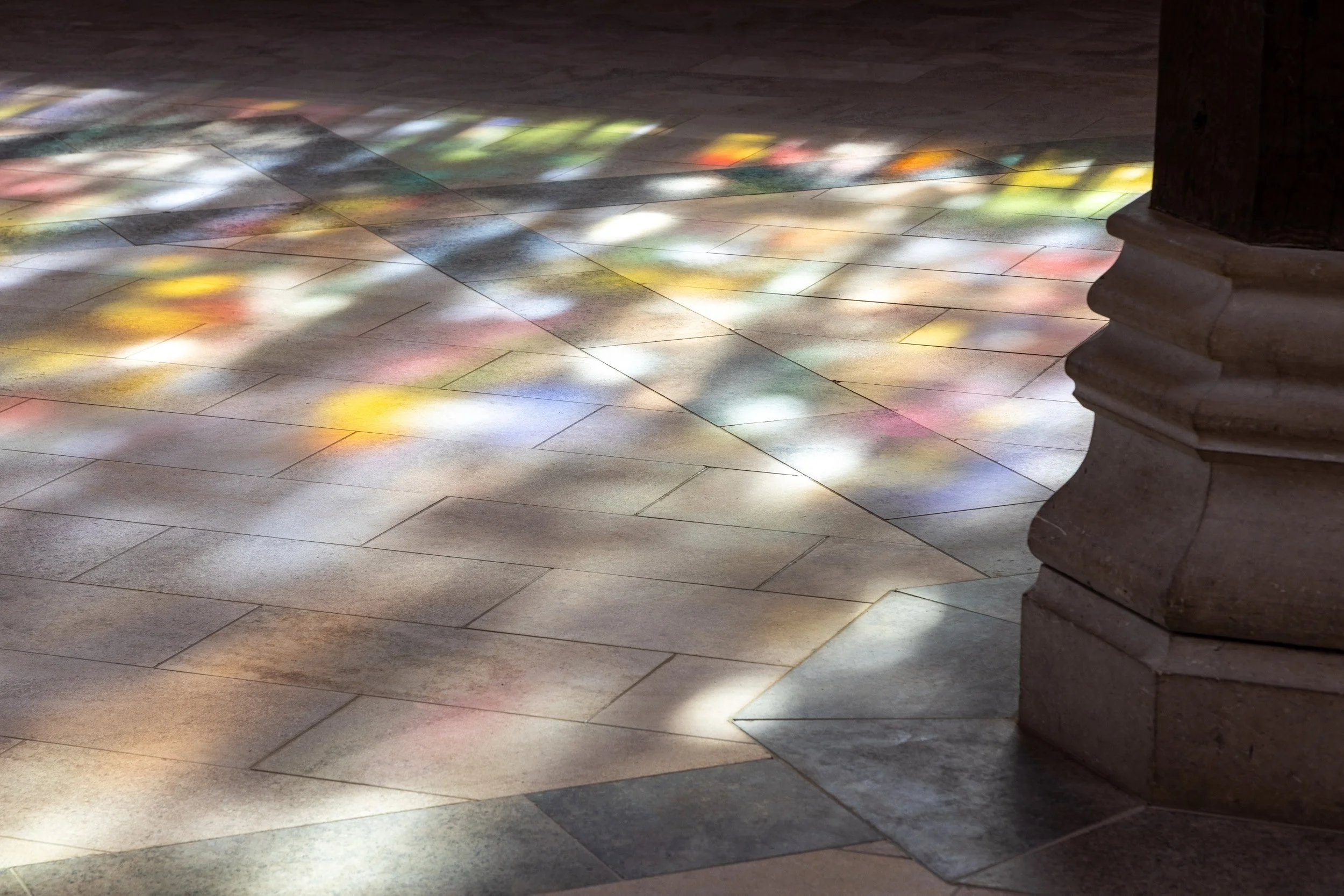 Sunlight shining through stained glass windows onto a tiled floor, creating colorful reflections.
