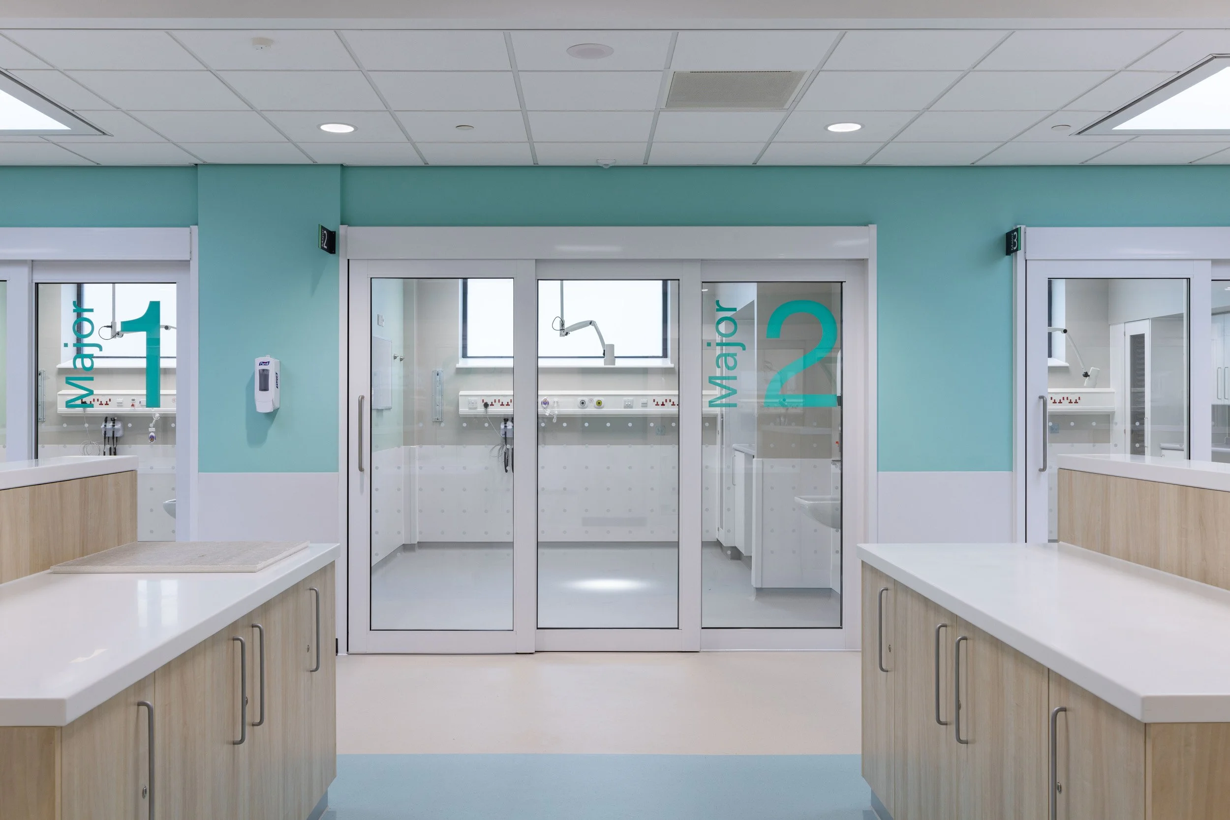 Hospital pediatric ward with two doors labeled Major 1 and Major 2, medical equipment inside, light blue walls, and light-colored countertops.