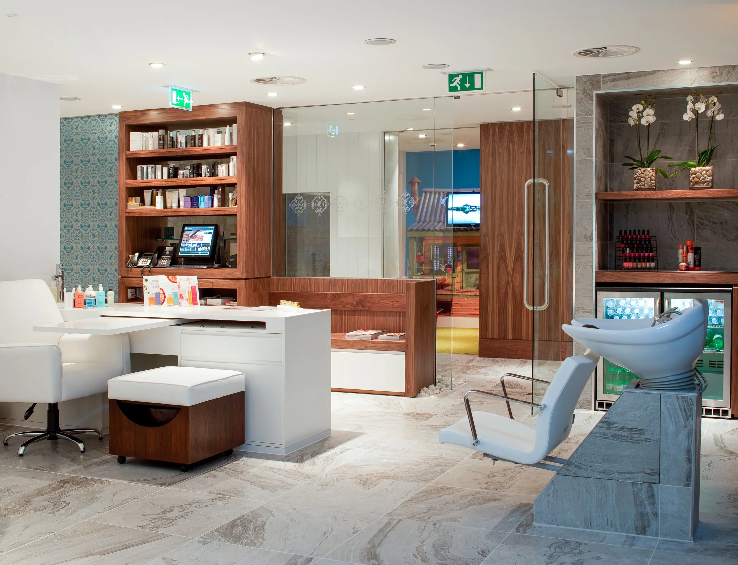 Salon with beauty station, massage chair, and hair washing basin, decorated with wood and marble accents.