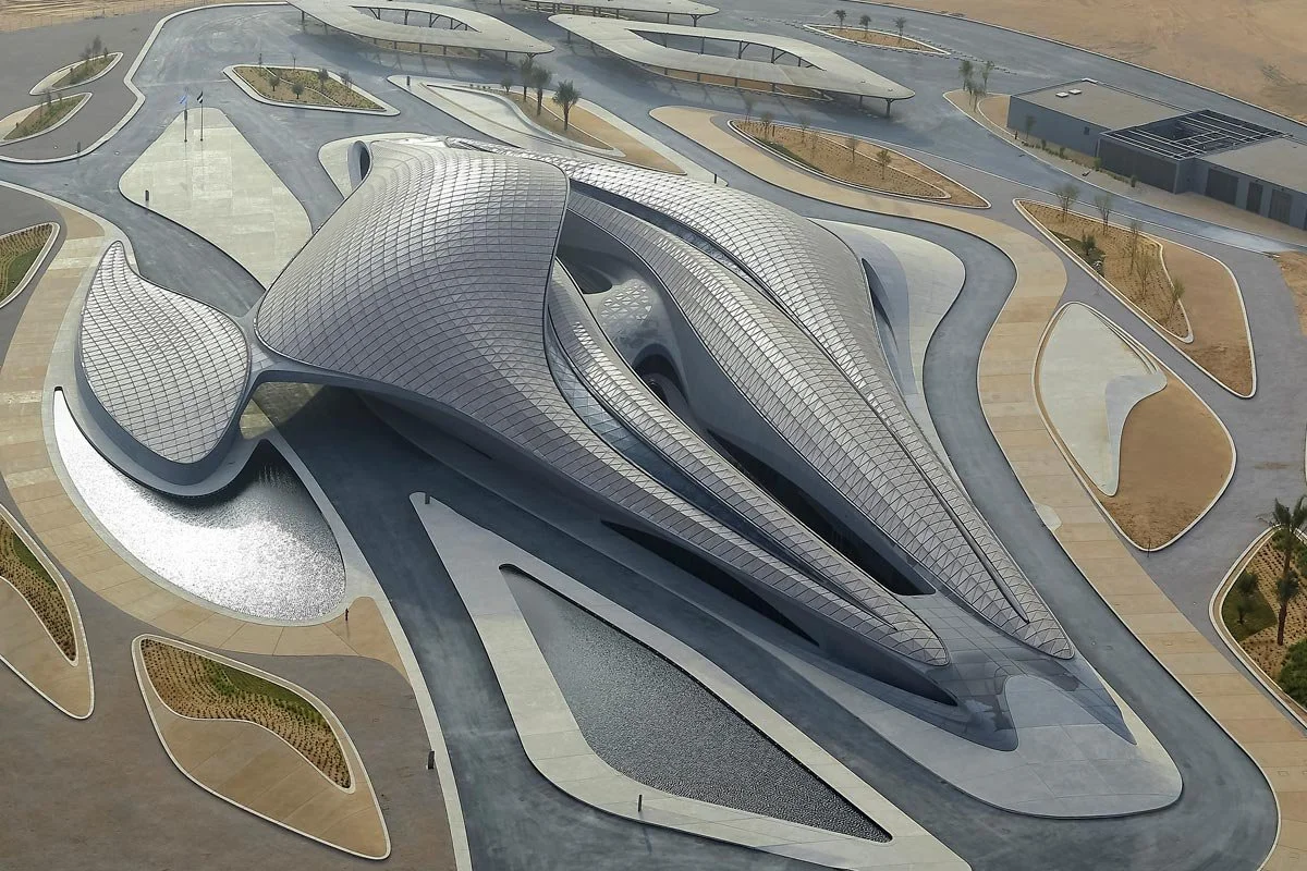 A modern, futuristic building with sleek, metallic, and curved architectural design, surrounded by landscaped pathways and small plant beds.