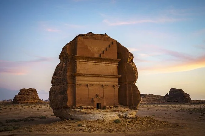 Ancient rock-cut tomb in desert landscape at sunset.