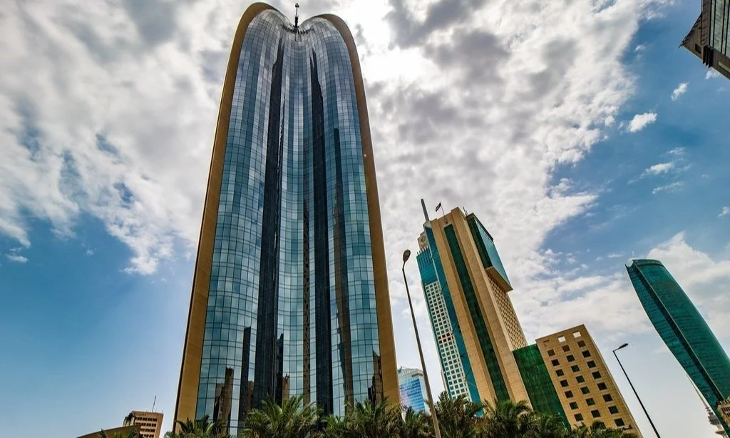 Tall glass skyscraper with curved top reflecting the sky and surrounding buildings in downtown.