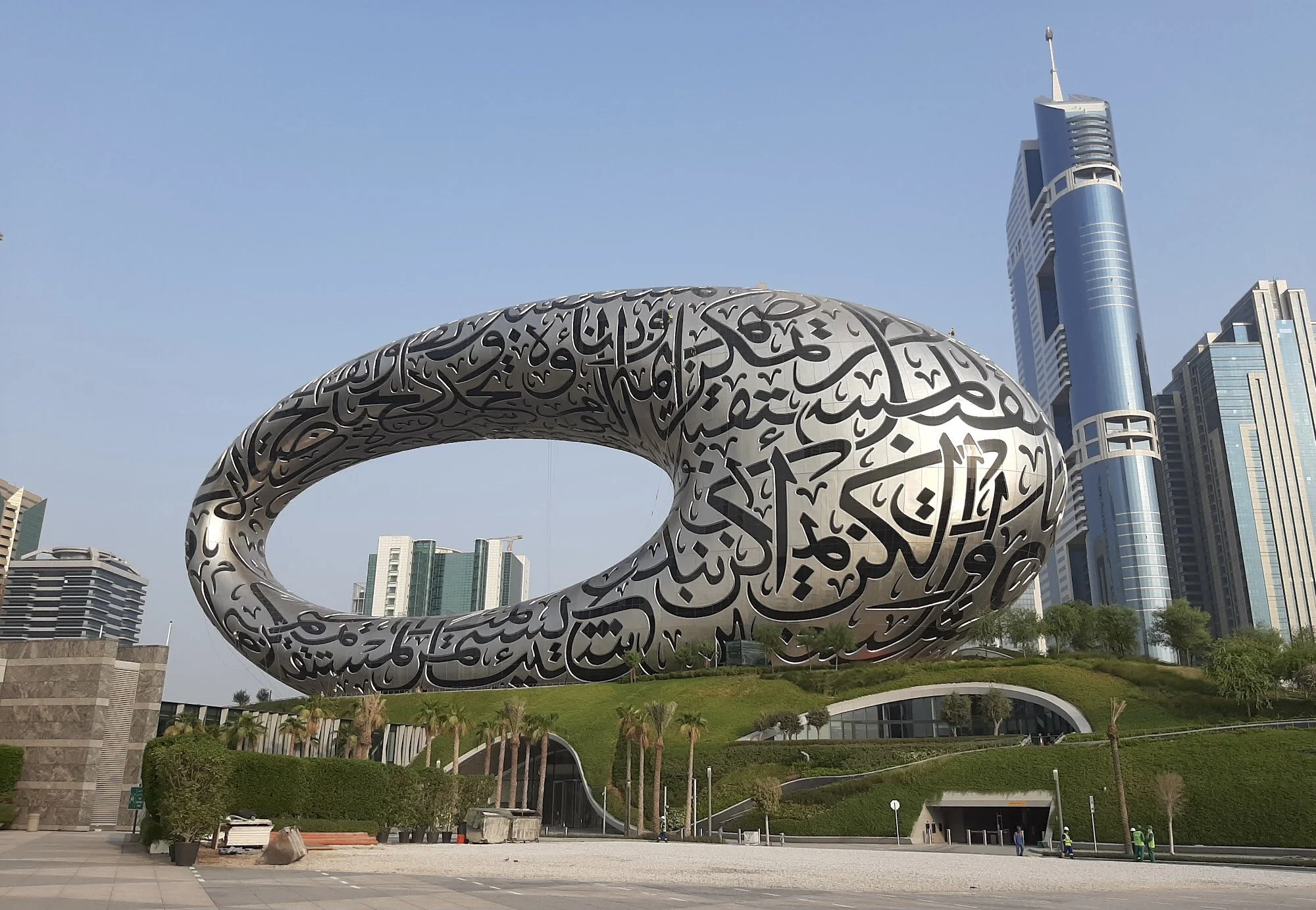 A modern city skyline featuring the Museum of the Future in Dubai, United Arab Emirates, with a distinctive torus-shaped exterior covered in Arabic calligraphy.
