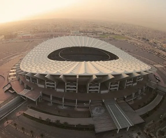 Aerial view of a large, modern stadium during sunset with a distinctive oval shape.